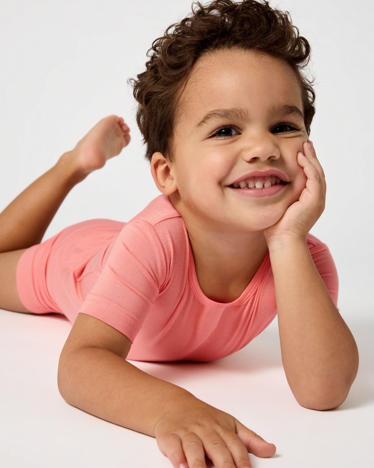 Child laying on a white surface wearing the Sweet Papaya Two-Piece Short Sleeve & Shorts Pajama Set
