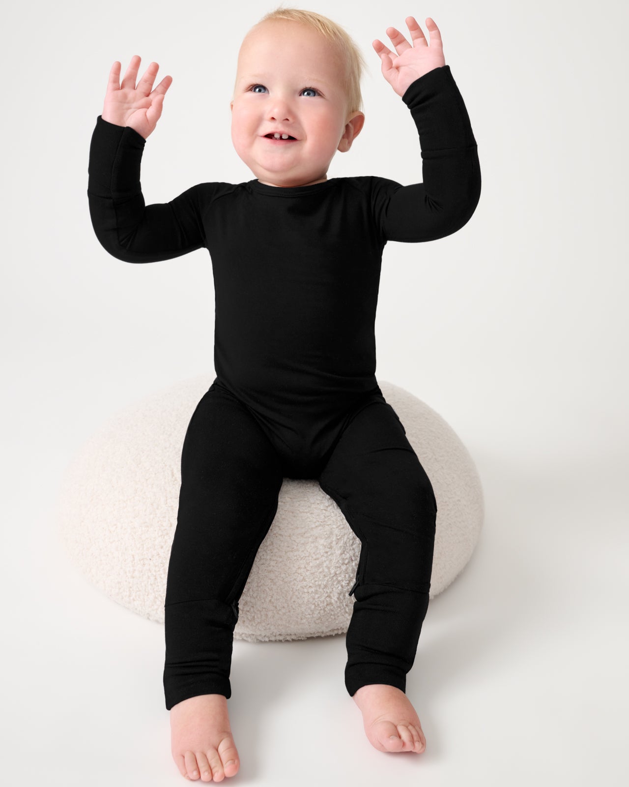 Baby sitting on a boucle cushion wearing the Black Crescent Zippy