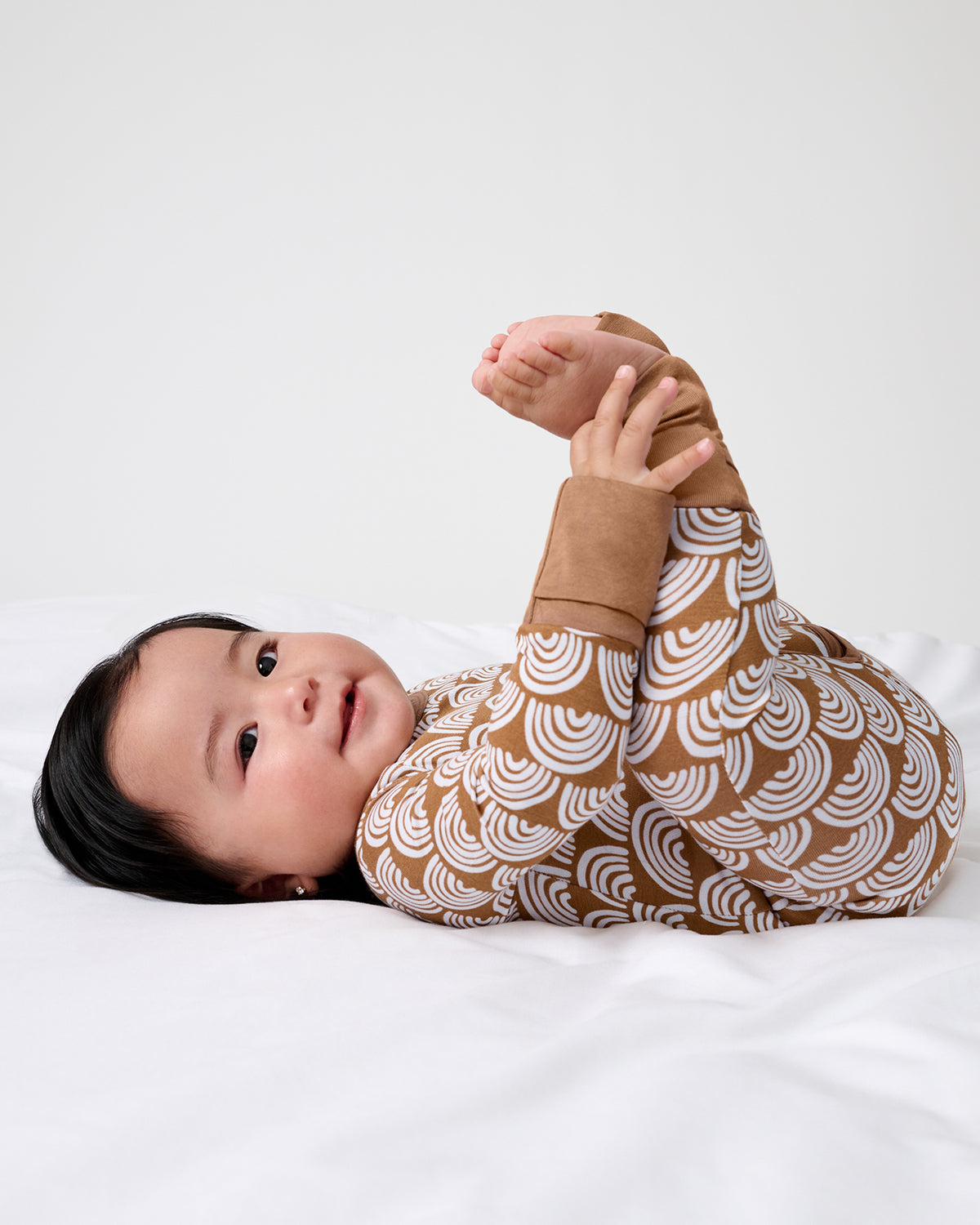 Baby with her feet in the air wearing the Rust Rainbows Crescent Zippy
