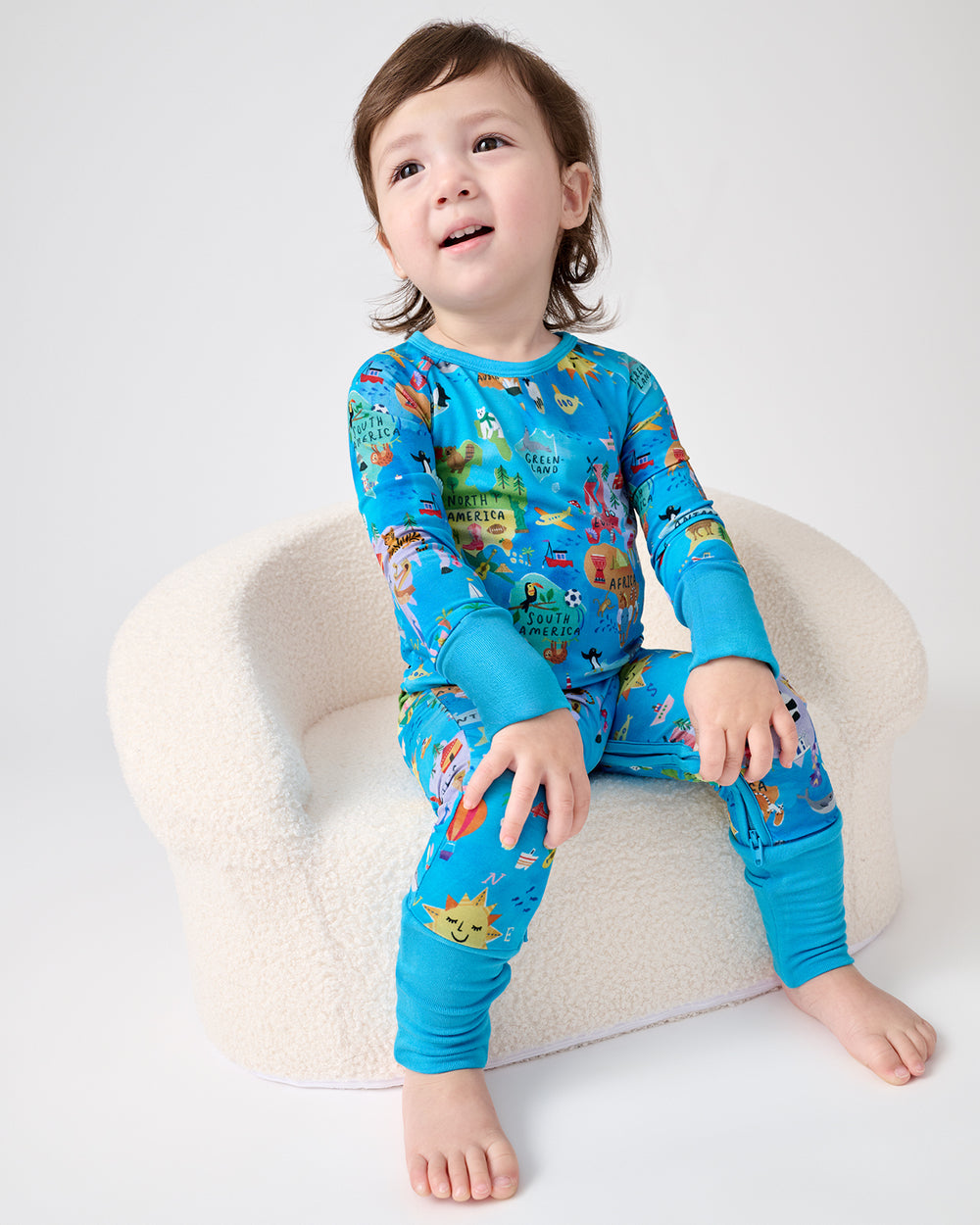 Toddler sitting on a boucle chair wearing the Around The World Crescent Zippy