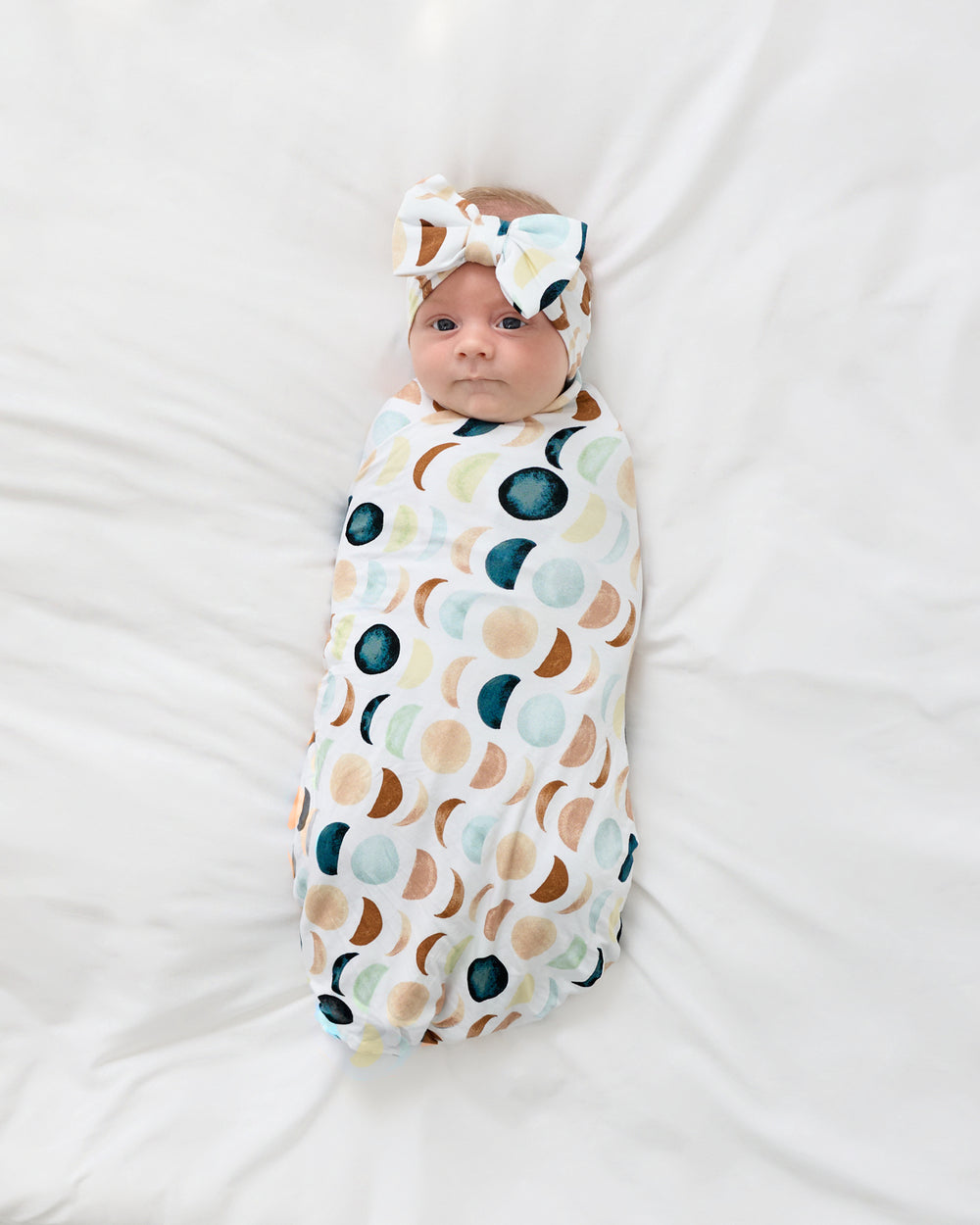 Aerial view of newborn wrapped in the Luna Neutral Swaddle & Luxe Bow Headband Set