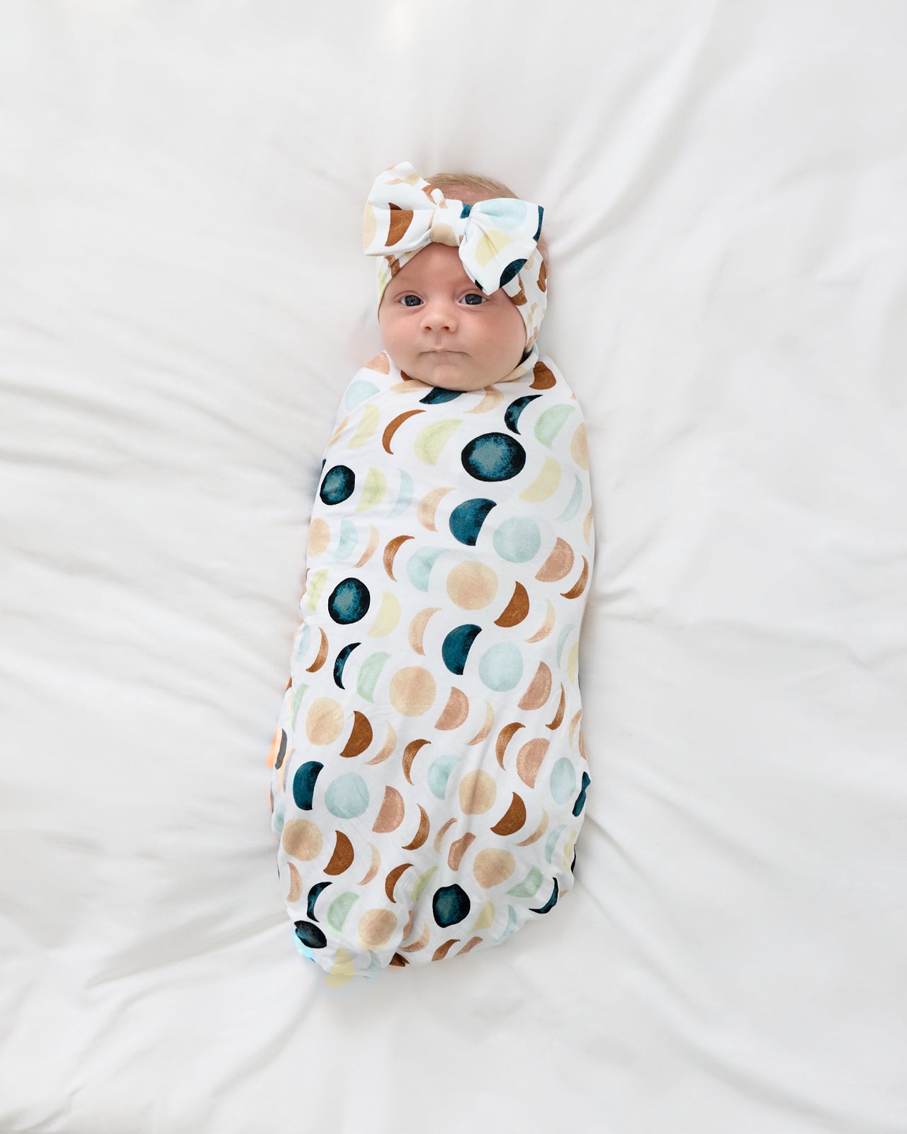 Aerial view of newborn wrapped in the Luna Neutral Swaddle & Luxe Bow Headband Set
