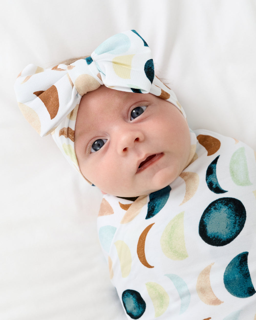 Close up of newborn swaddled in the Luna Neutral Swaddle & Luxe Bow Headband Set