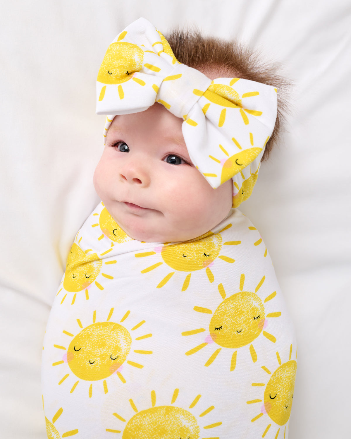 Close up of newborn wrapped in the Sunshine Swaddle & Luxe Bow Headband Set