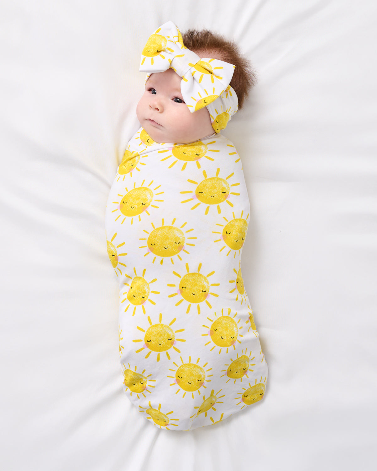 Aerial view of newborn swaddled in the Sunshine Swaddle & Luxe Bow Headband Set