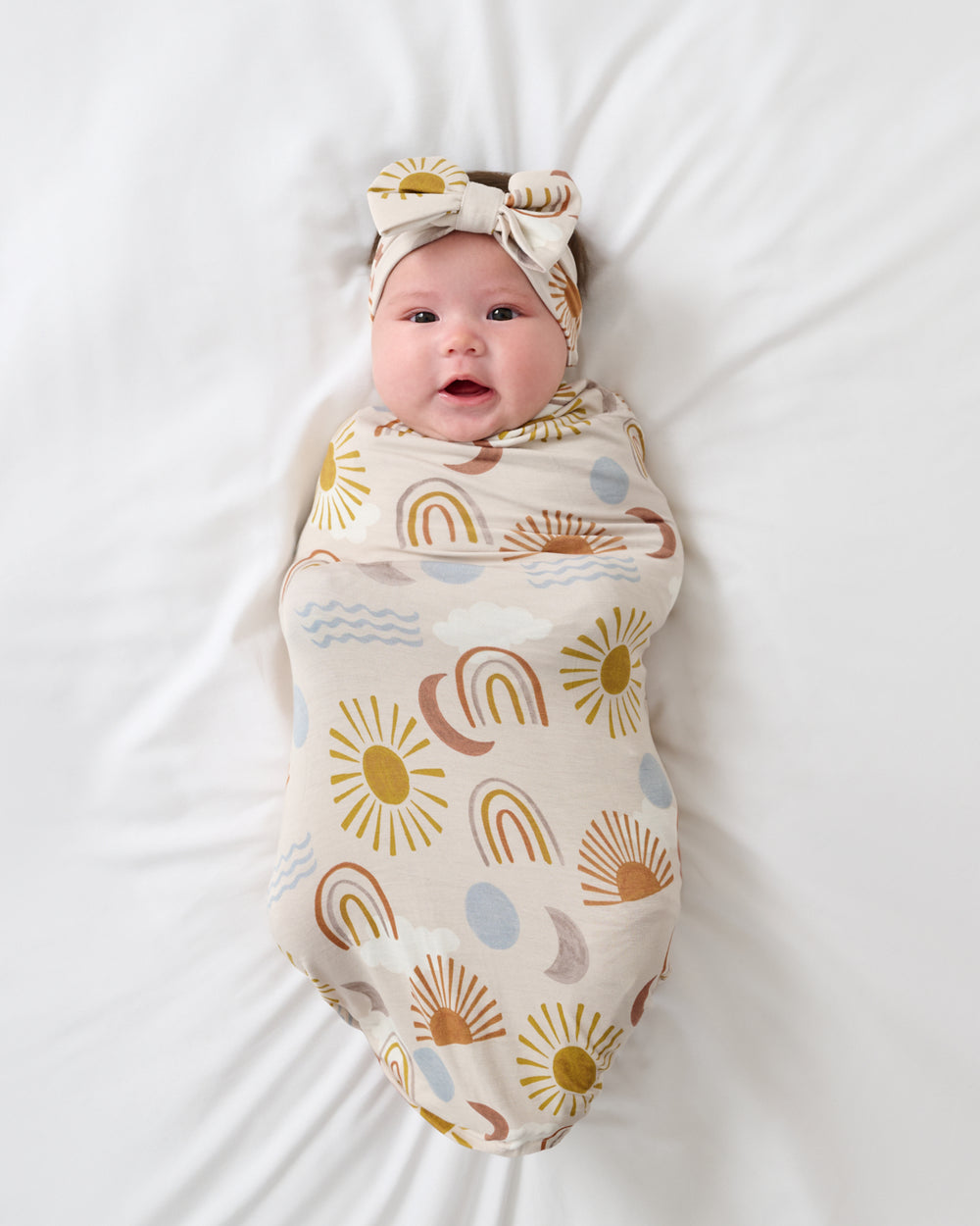 Aerial view of baby wrapped in the Desert Sunrise Swaddle & Luxe Bow Headband Set