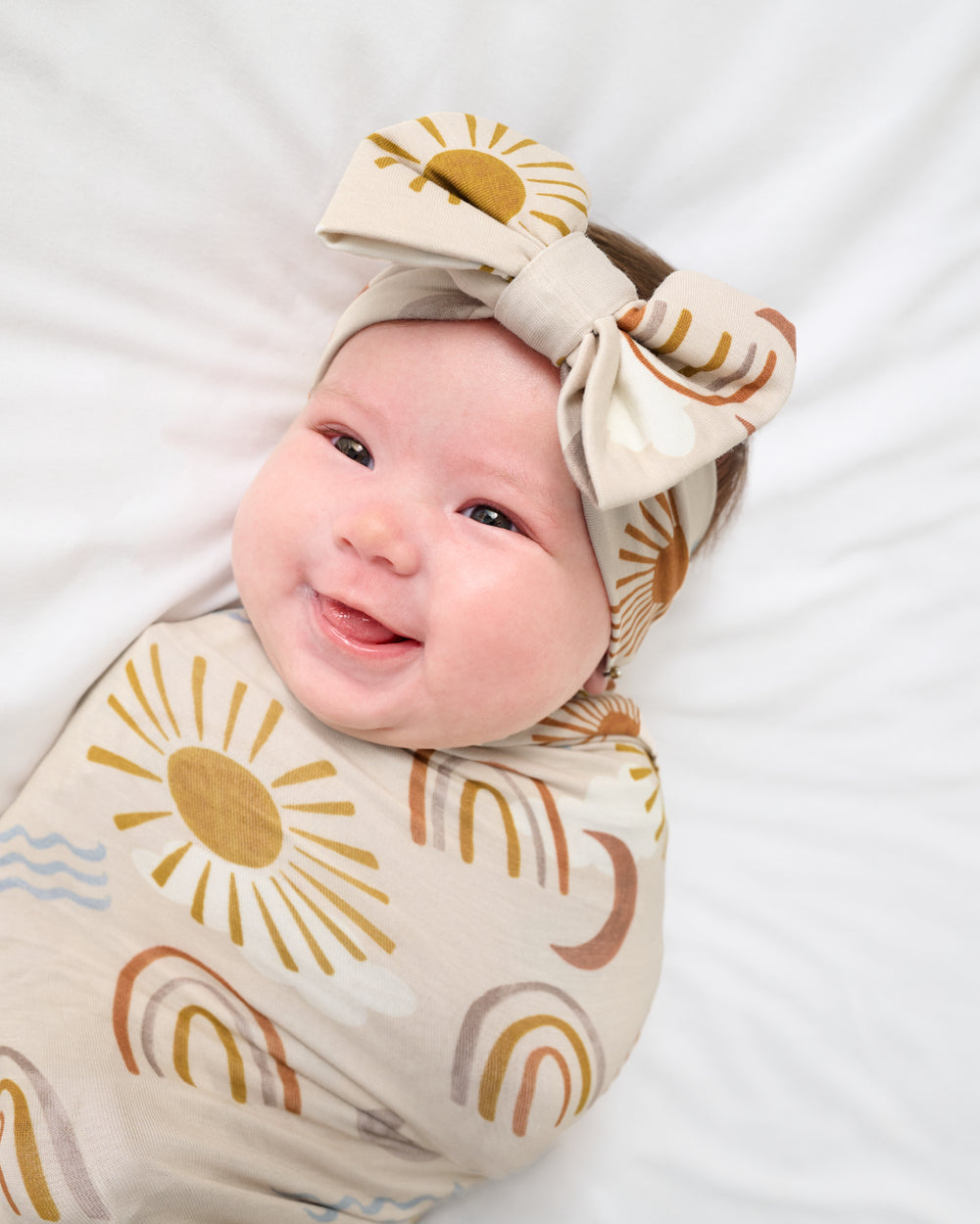 Close up of baby wearing the Desert Sunrise Swaddle & Luxe Bow Headband Set