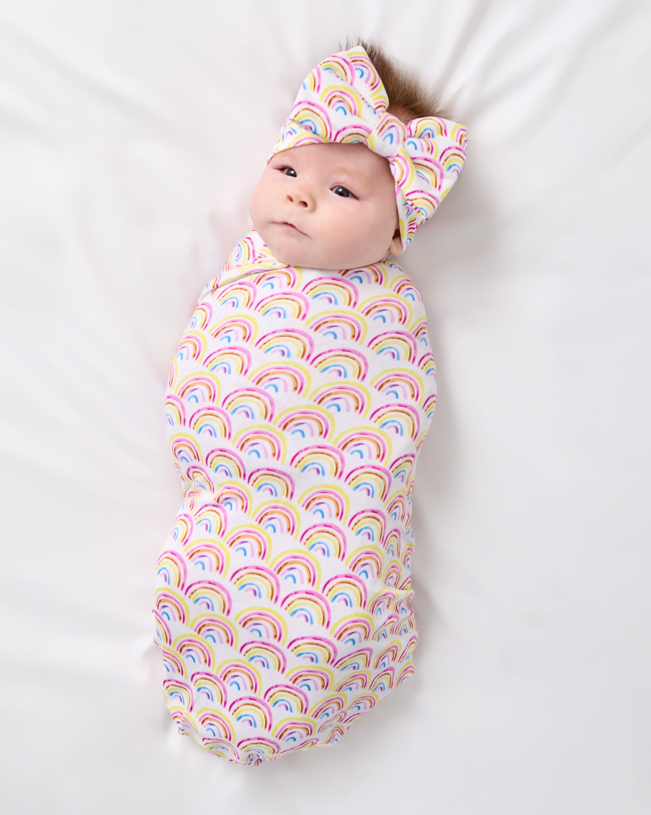 Aerial view of baby wearing the Pastel Rainbows Swaddle & Luxe Bow Headband Set