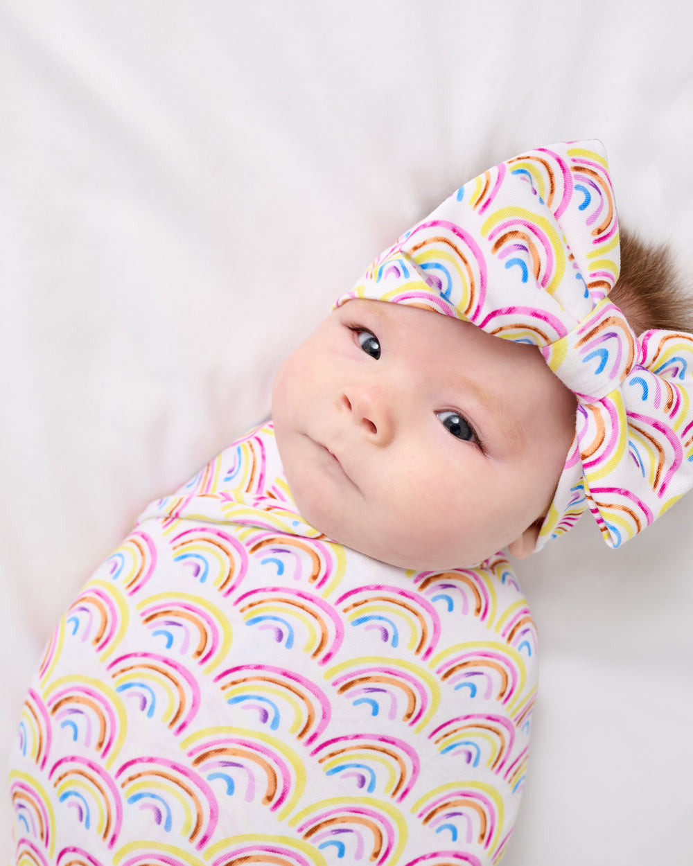 Close up of newborn wrapped in the Pastel Rainbows Swaddle & Luxe Bow Headband Set