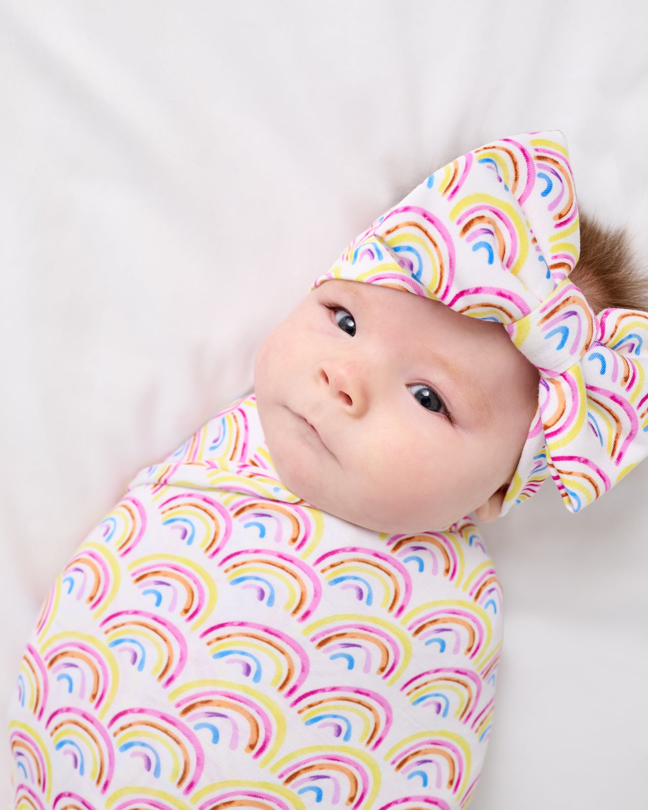 Close up of newborn wrapped in the Pastel Rainbows Swaddle & Luxe Bow Headband Set
