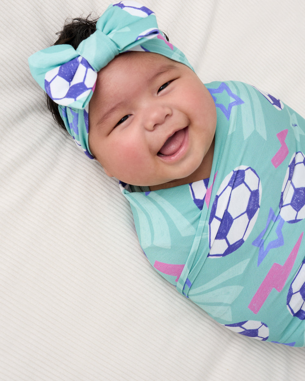 Close up of baby wearing the Aqua Soccer Stars Swaddle & Luxe Bow Headband Set