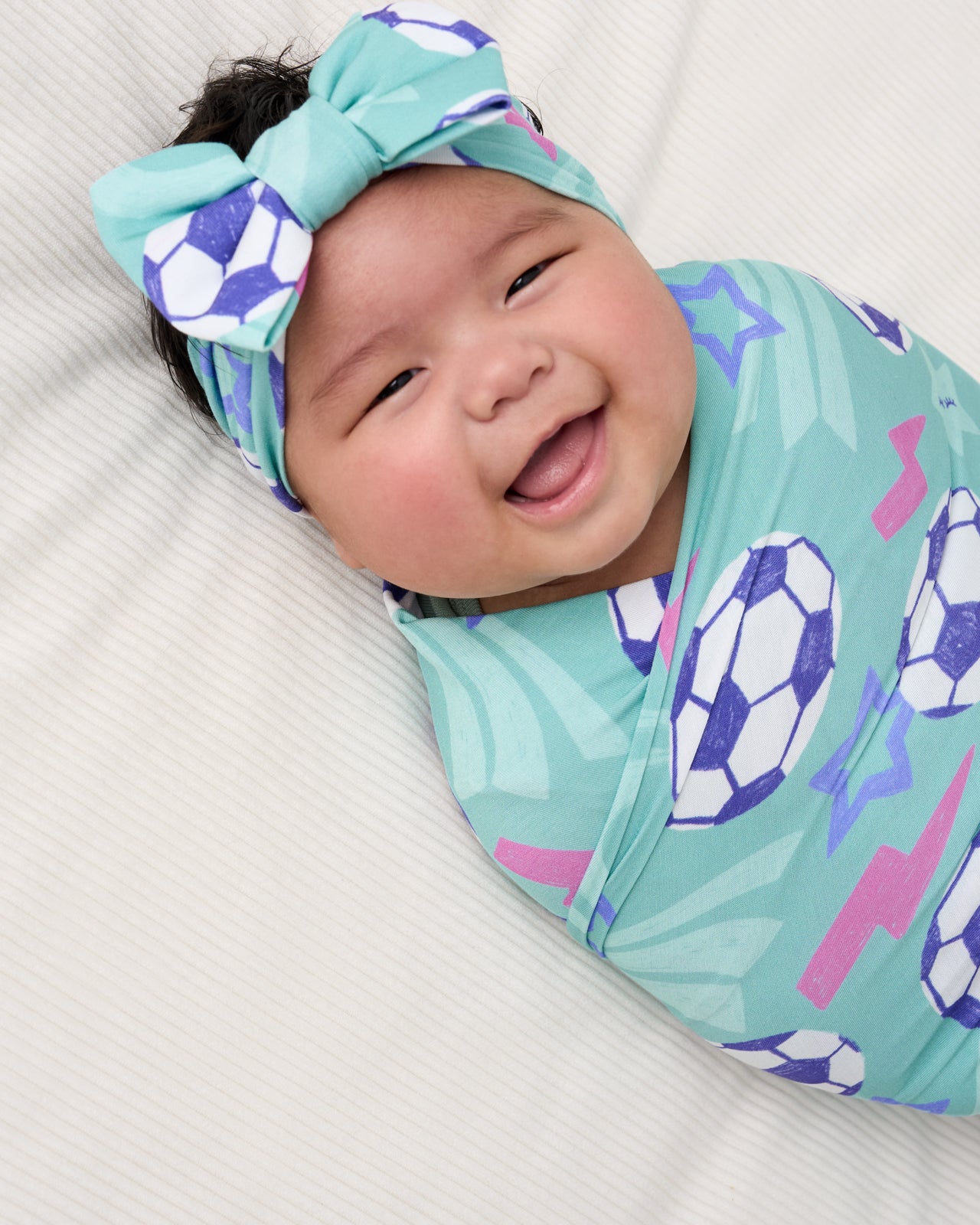 Close up of baby wearing the Aqua Soccer Stars Swaddle & Luxe Bow Headband Set