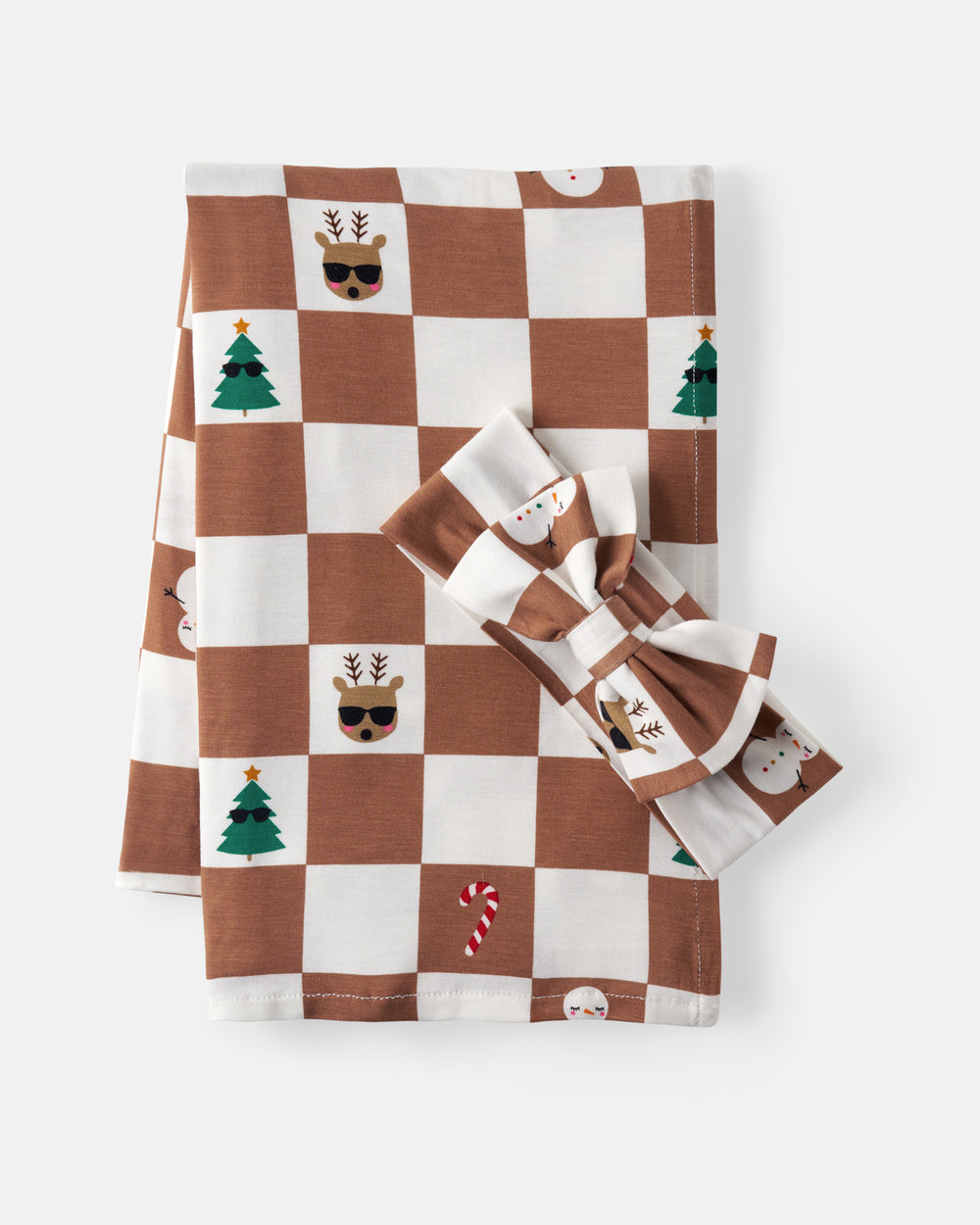 A folded swaddling blanket, with a matching bow, featuring a brown and white checkerboard pattern decorated with Christmas-themed illustrations including trees, candy canes, and reindeer.