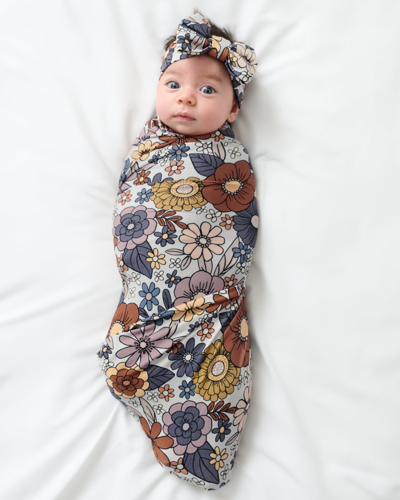 Aerial view of baby wearing the Wildwood Floral Swaddle & Luxe Bow Headband Set
