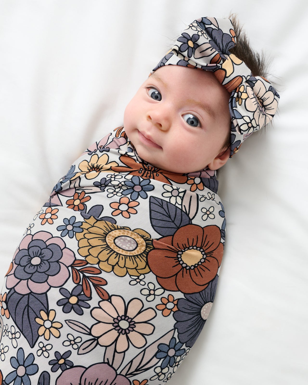 Close up of baby swaddled in the Wildwood Floral Swaddle & Luxe Bow Headband Set