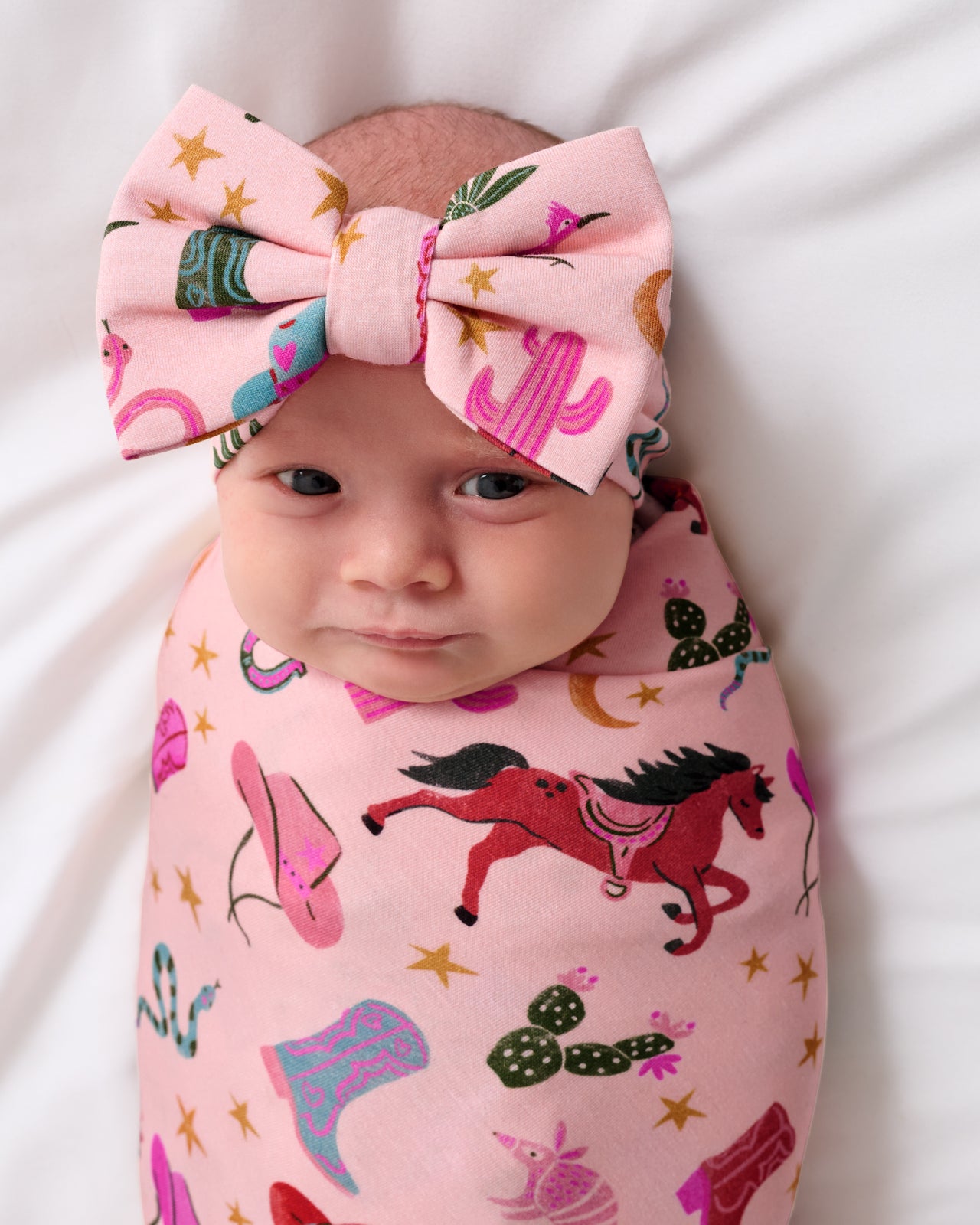 Close up of baby in the Pink Rancher Roundup Swaddle & Luxe Bow Headband Set