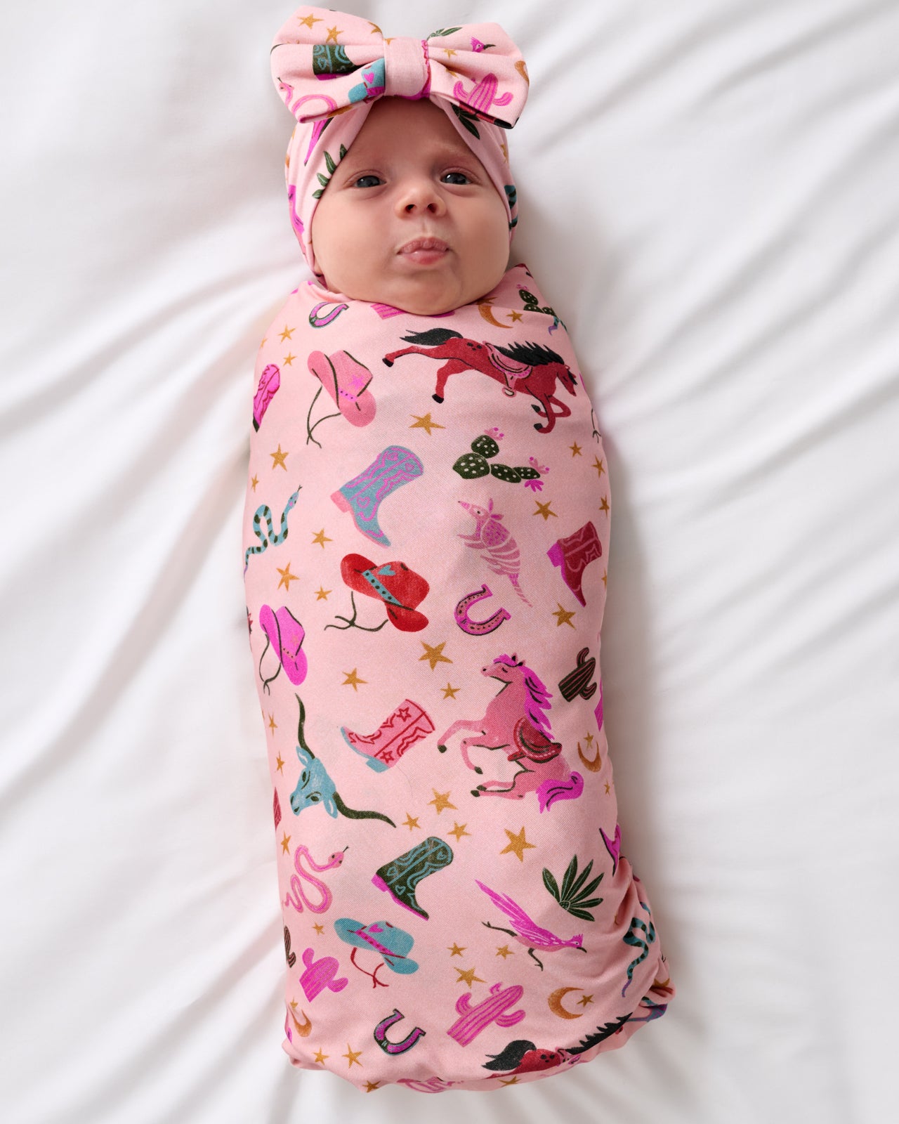 Aerial view of baby wrapped in the Pink Rancher Roundup Swaddle & Luxe Bow Headband Set
