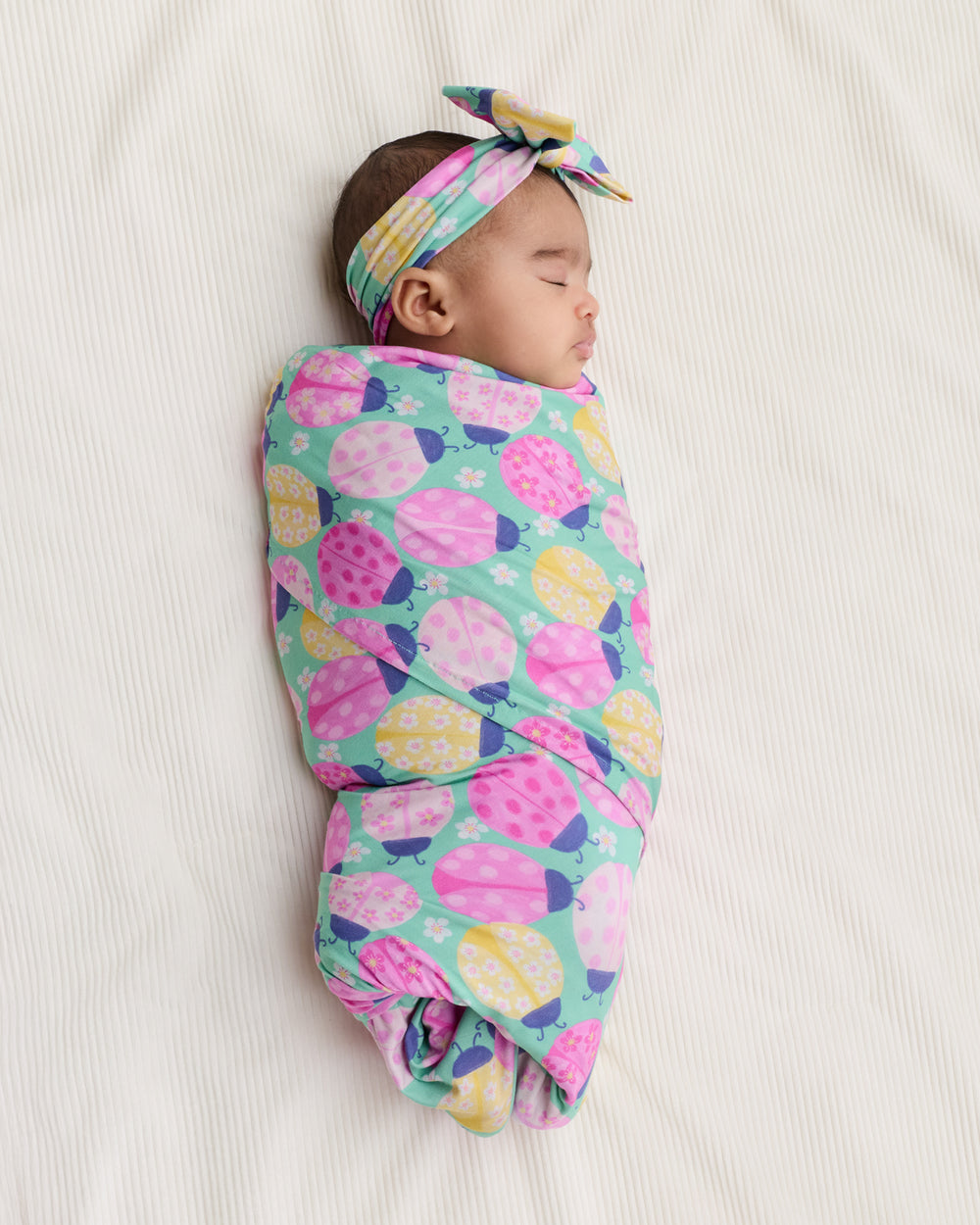 Aerial view of baby wearing the Ladybug Meadow Swaddle & Luxe Bow Headband Set
