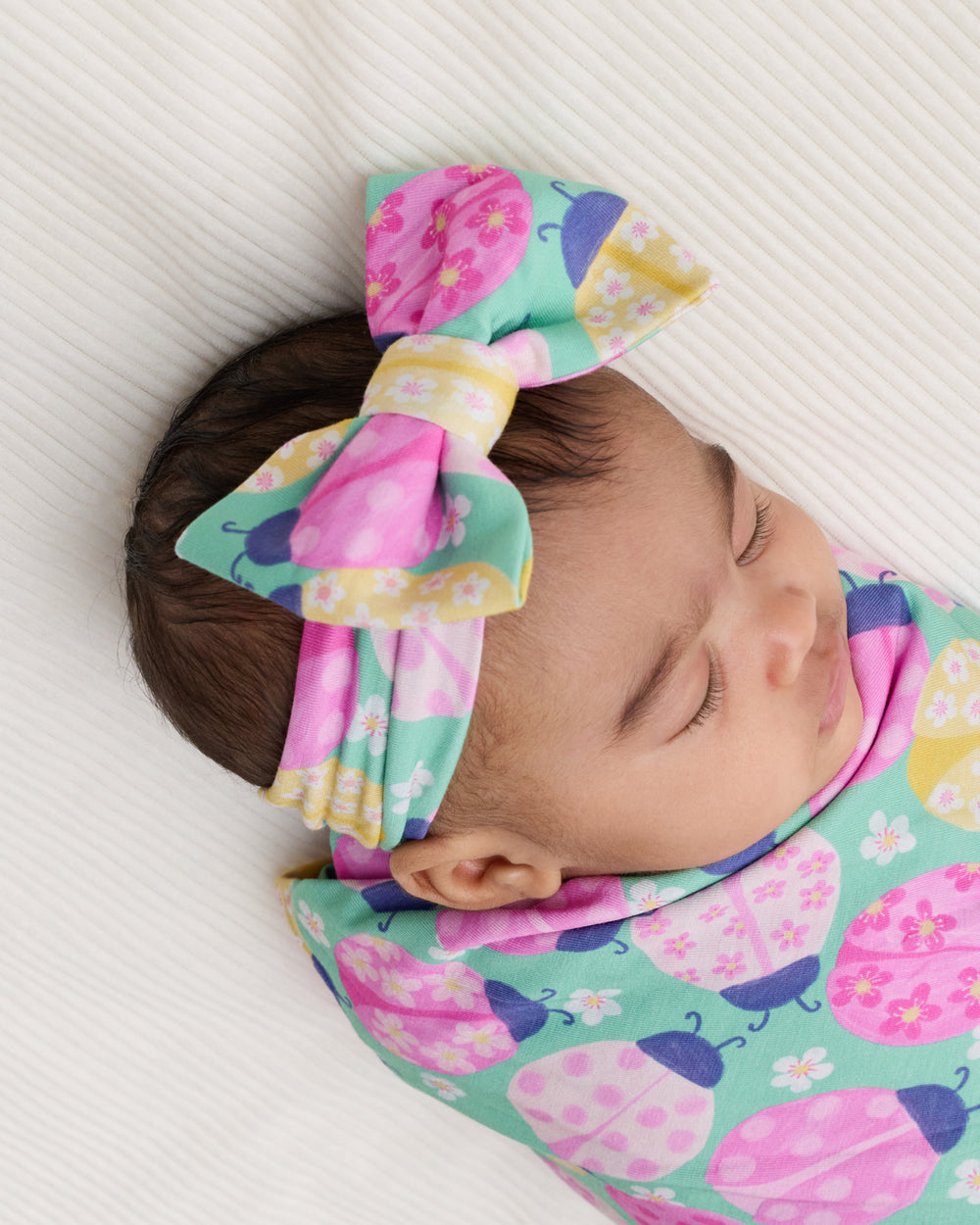 Close up of newborn wrapped in the Ladybug Meadow Swaddle & Luxe Bow Headband Set 