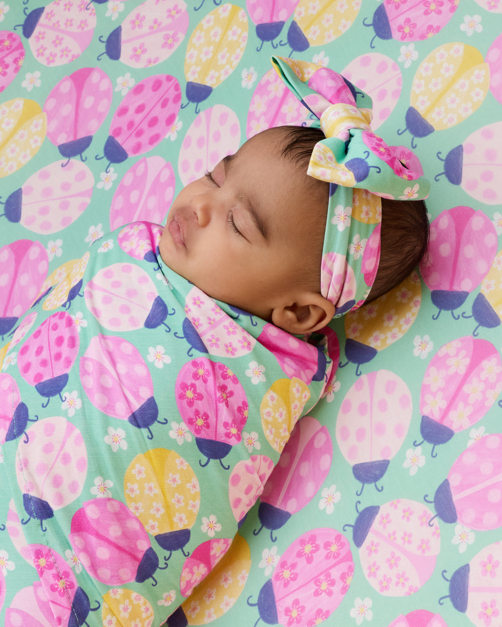 Sleeping newborn laying on the Ladybug Meadow Fitted Crib Sheet 