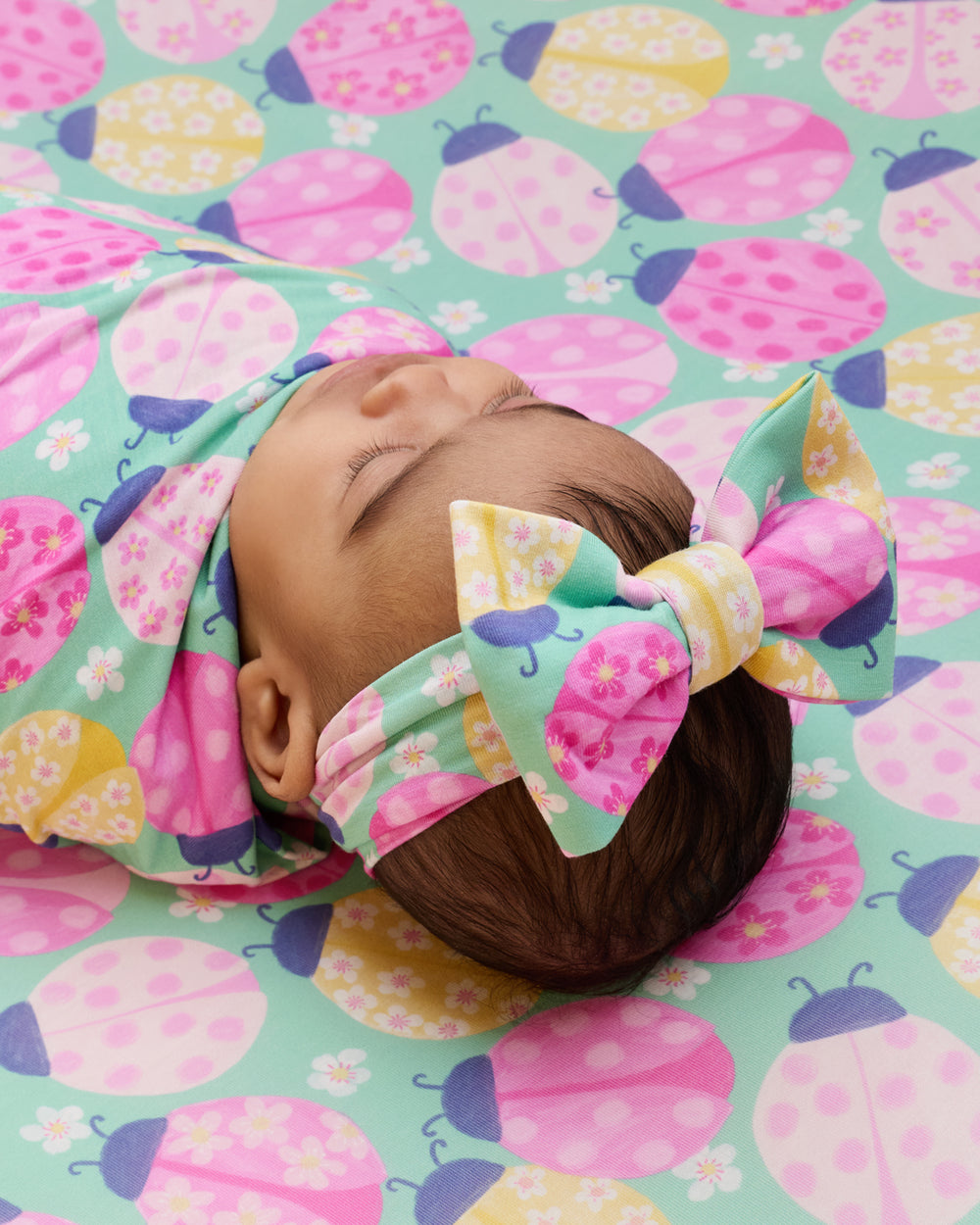 Close up of newborn wrapped in the Ladybug Meadow Swaddle & Luxe Bow Headband Set