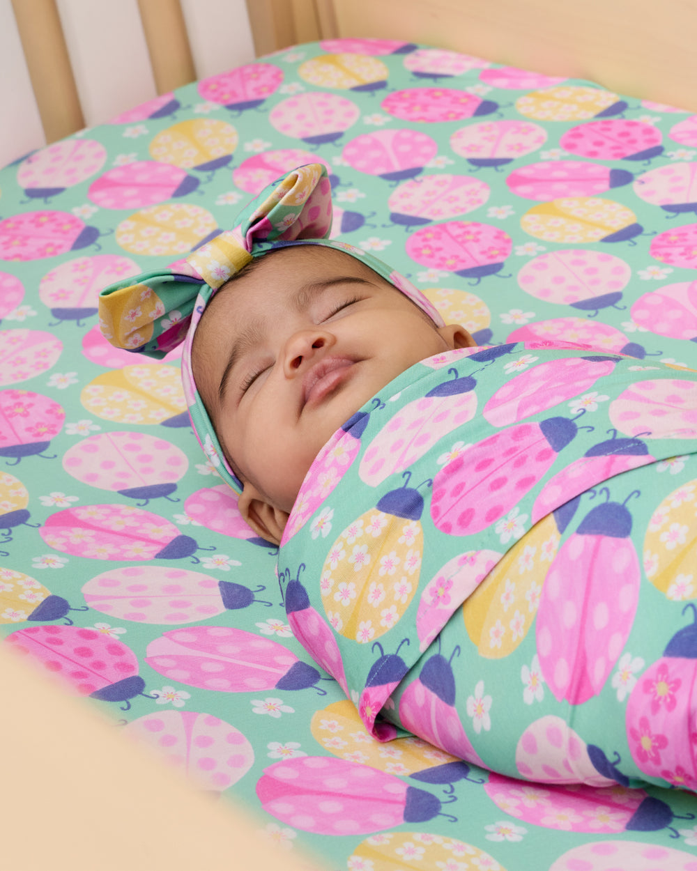 Swaddled baby in a crib with the Ladybug Meadow Fitted Crib Sheet