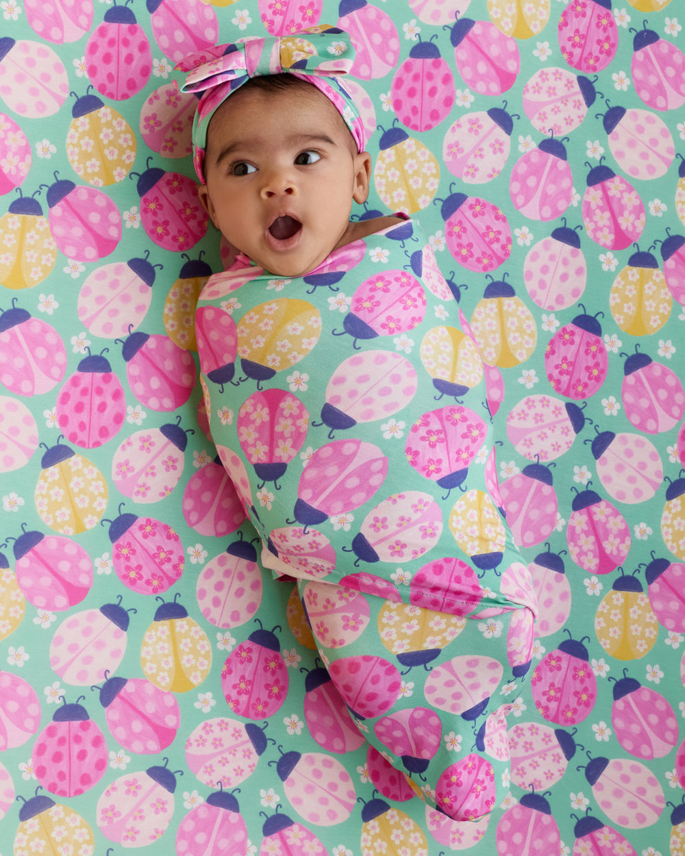 Aerial view of baby swaddled in the Ladybug Meadow Swaddle & Luxe Bow Headband Set