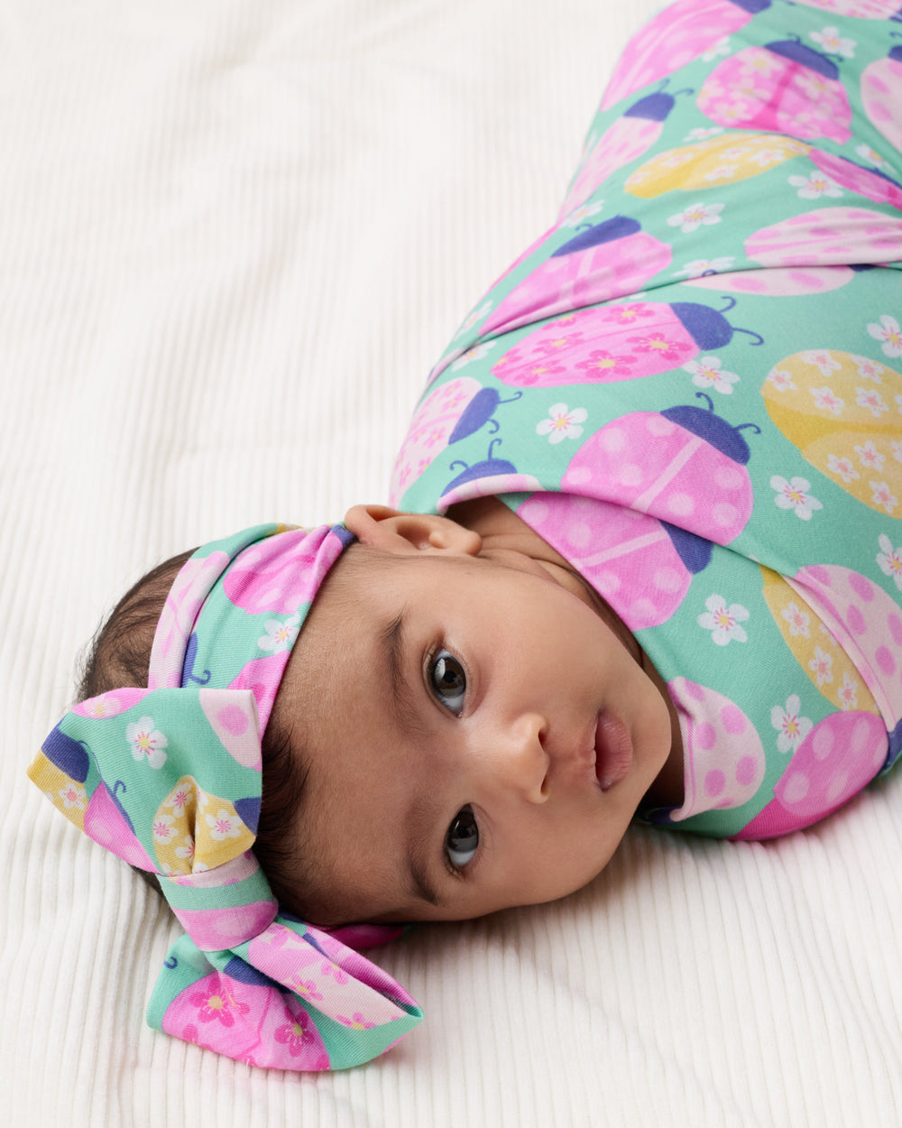 Newborn baby swaddled in the Ladybug Meadow Swaddle & Luxe Bow Headband Set