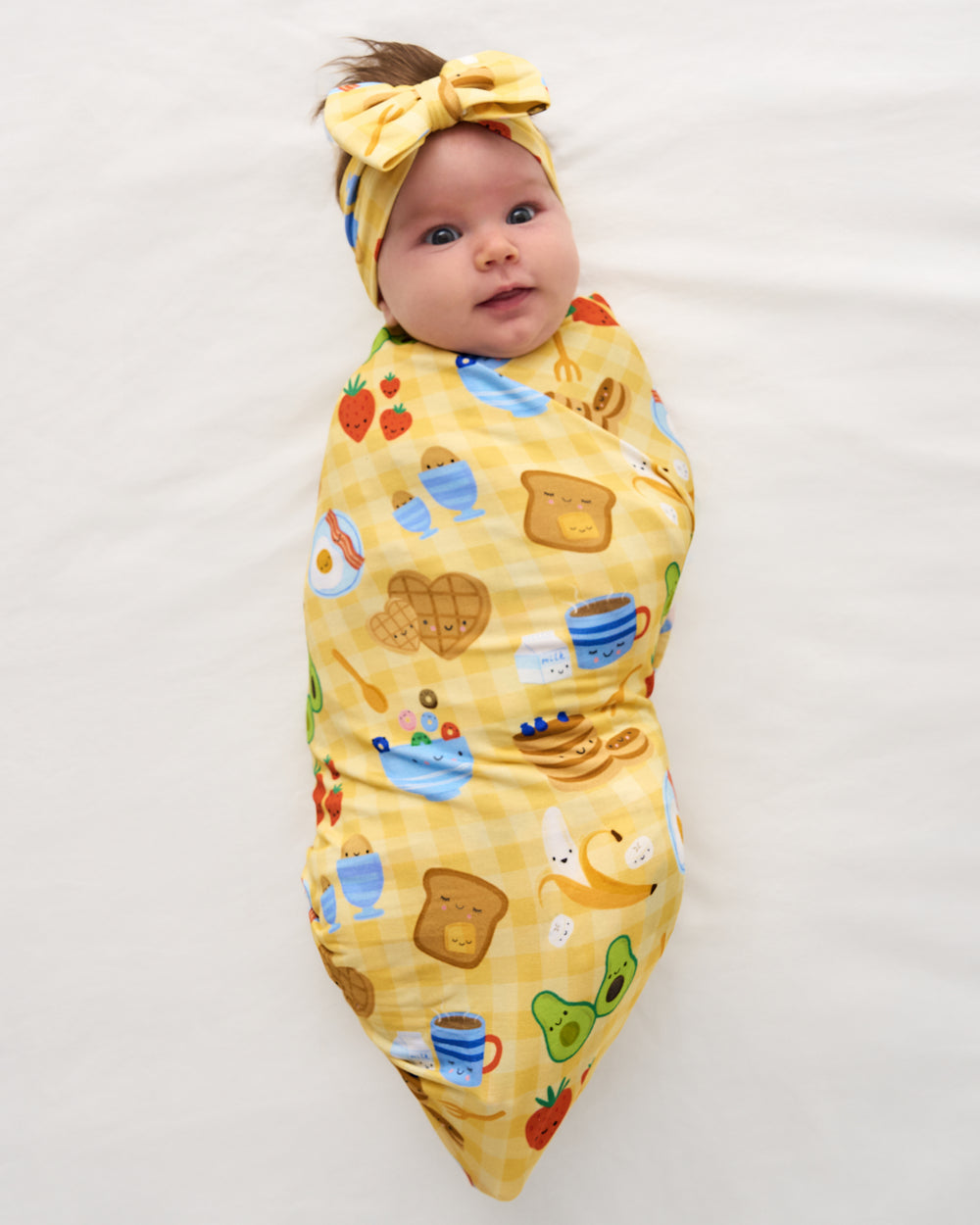 Aerial view of baby wearing the Breakfast Bunch Swaddle & Luxe Bow Headband Set