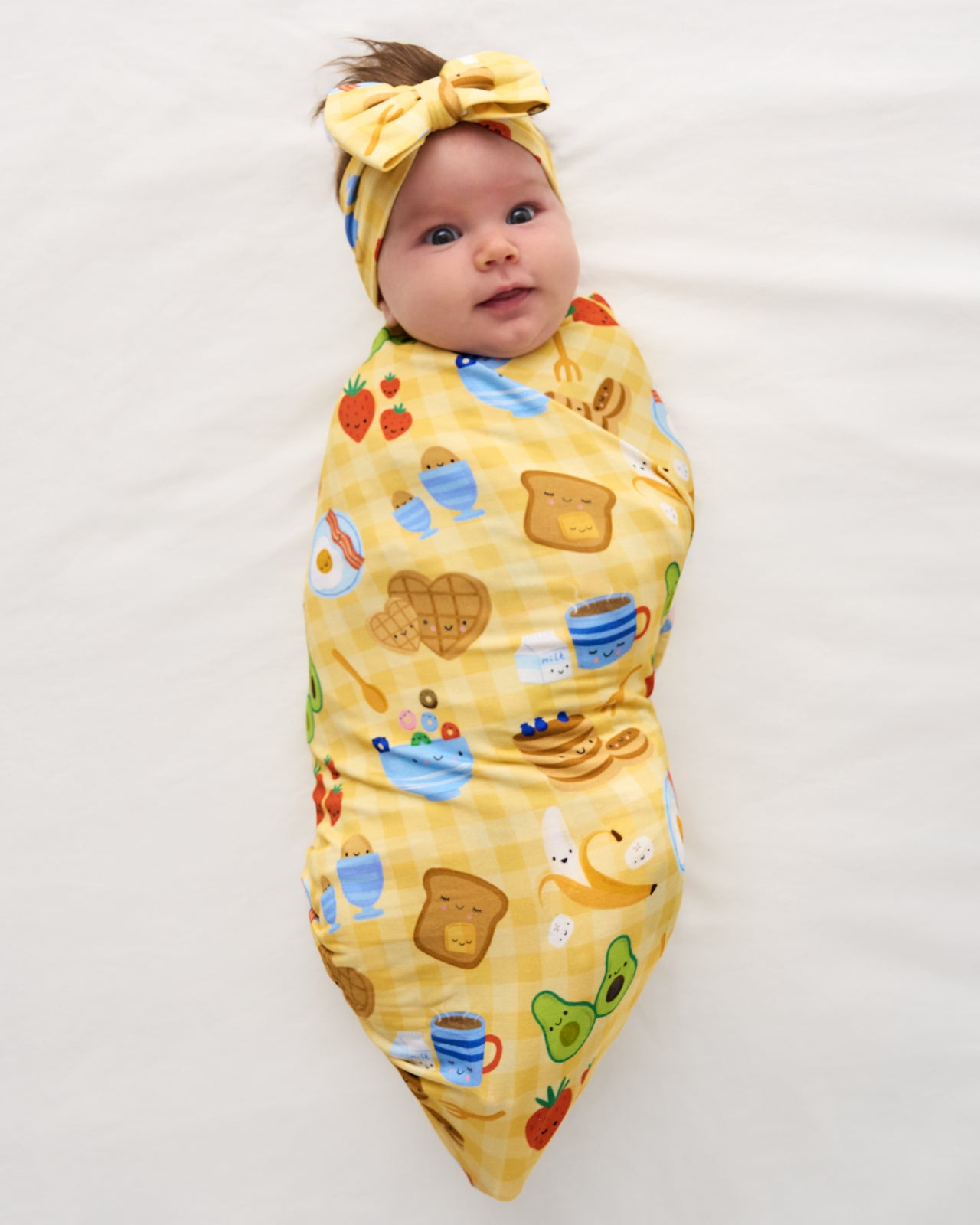 Aerial view of baby wearing the Breakfast Bunch Swaddle & Luxe Bow Headband Set