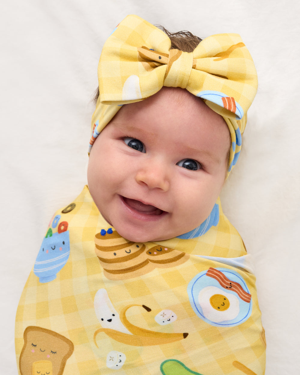Close up of baby wearing the Breakfast Bunch Swaddle & Luxe Bow Headband Set