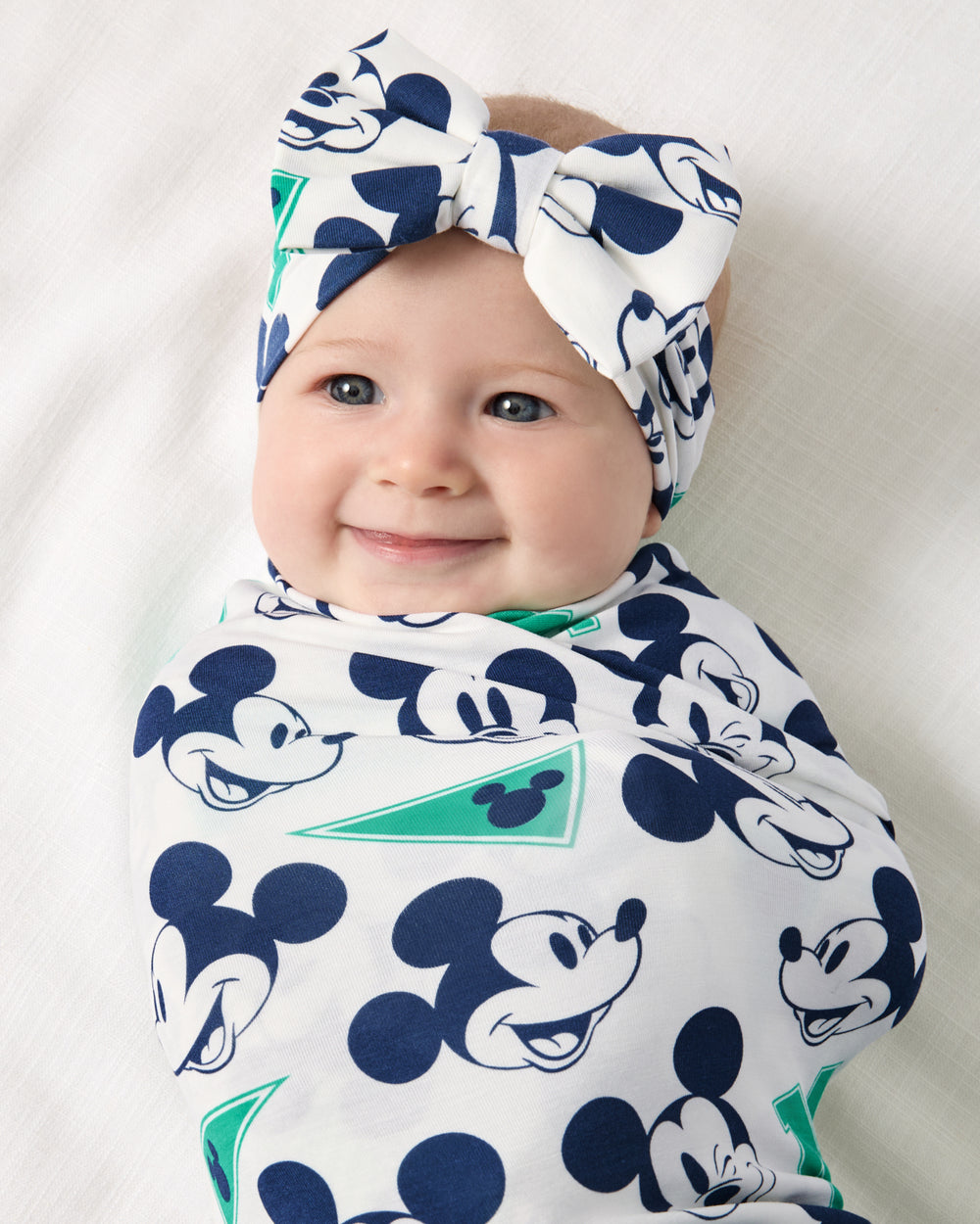Close up of baby wearing the Disney Varsity Mickey Mouse Swaddle & Luxe Bow Headband Set