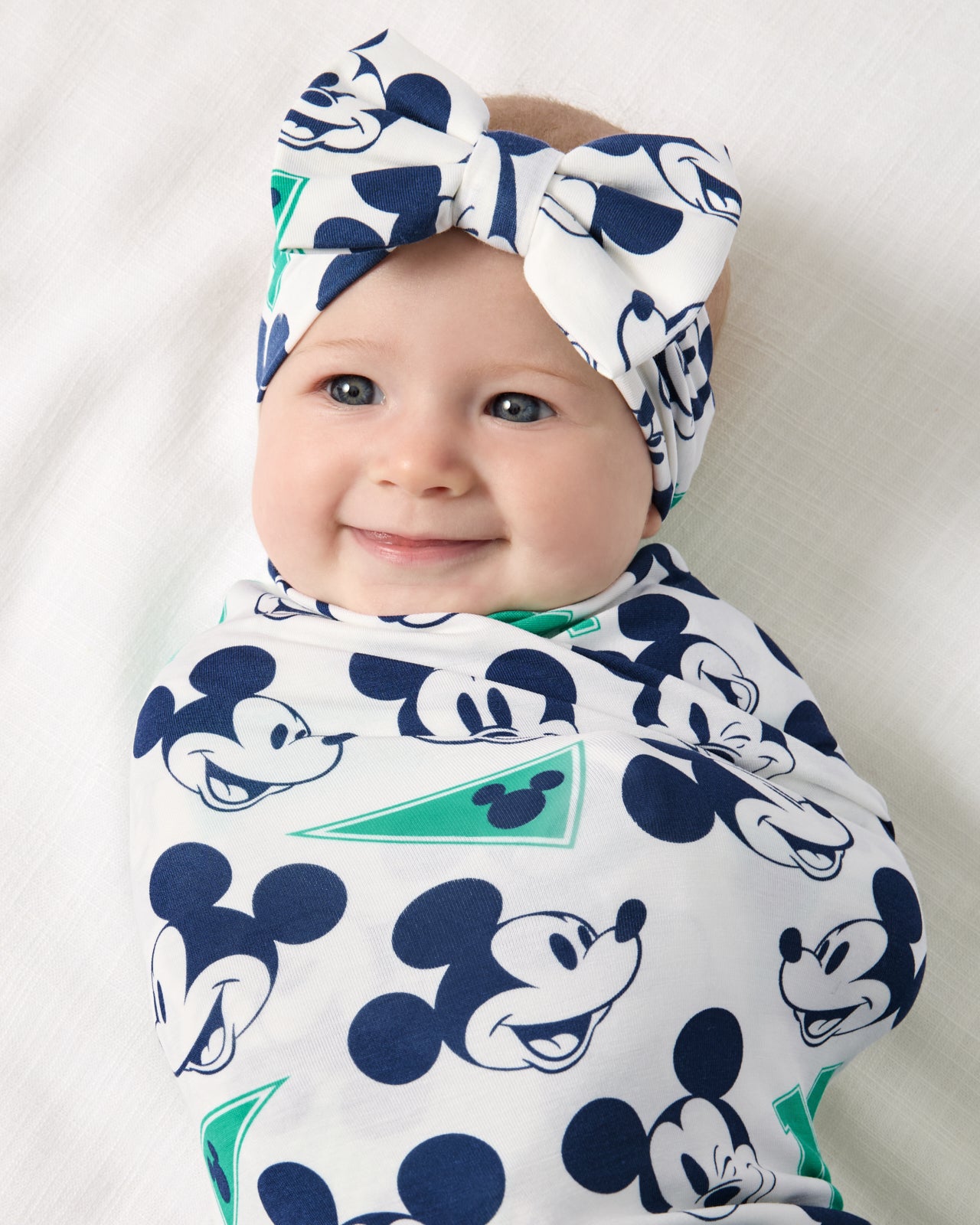 Close up of baby wearing the Disney Varsity Mickey Mouse Swaddle & Luxe Bow Headband Set