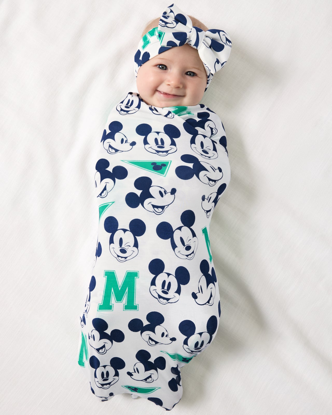 Aerial view of baby wearing the Disney Varsity Mickey Mouse Swaddle & Luxe Bow Headband Set