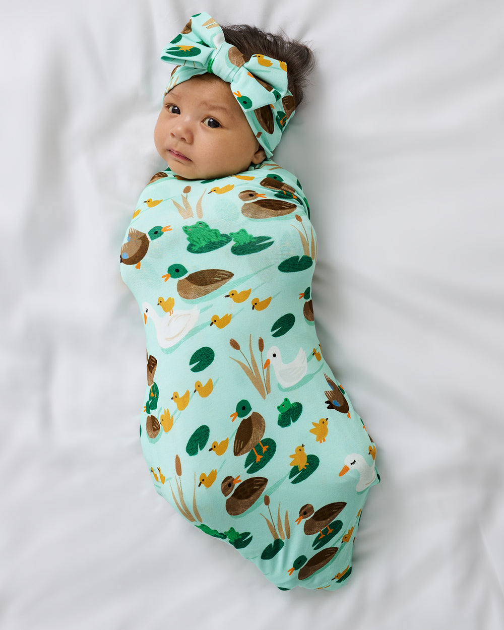 Aerial view of newborn wrapped in the Puddle Jumpers Swaddle & Luxe Bow Headband Set