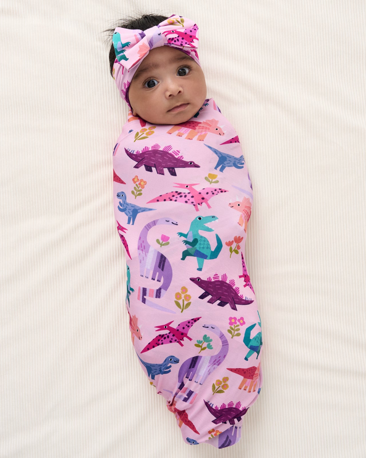 Aerial view of baby wrapped in the Pink Roar & Explore Swaddle & Luxe Bow Headband Set