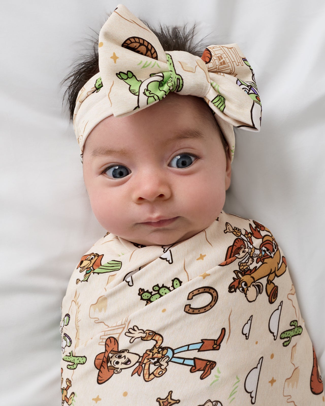 Close up of baby wrapped in the Disney & Pixar Woody's Wild West Swaddle & Luxe Bow Headband Set