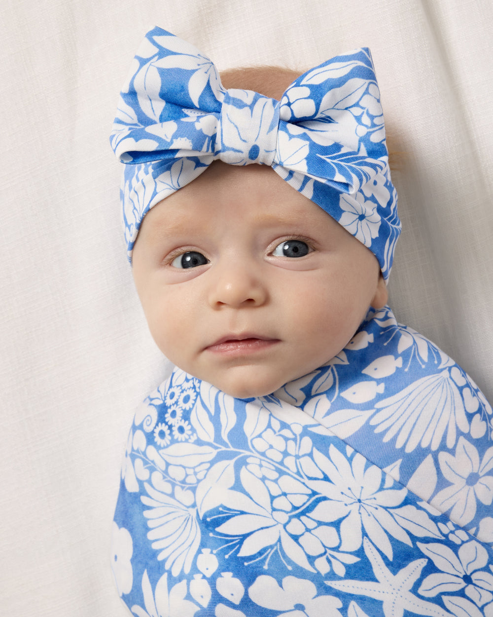 Close up of baby wrapped in the Azure Garden Swaddle & Luxe Bow Headband Set