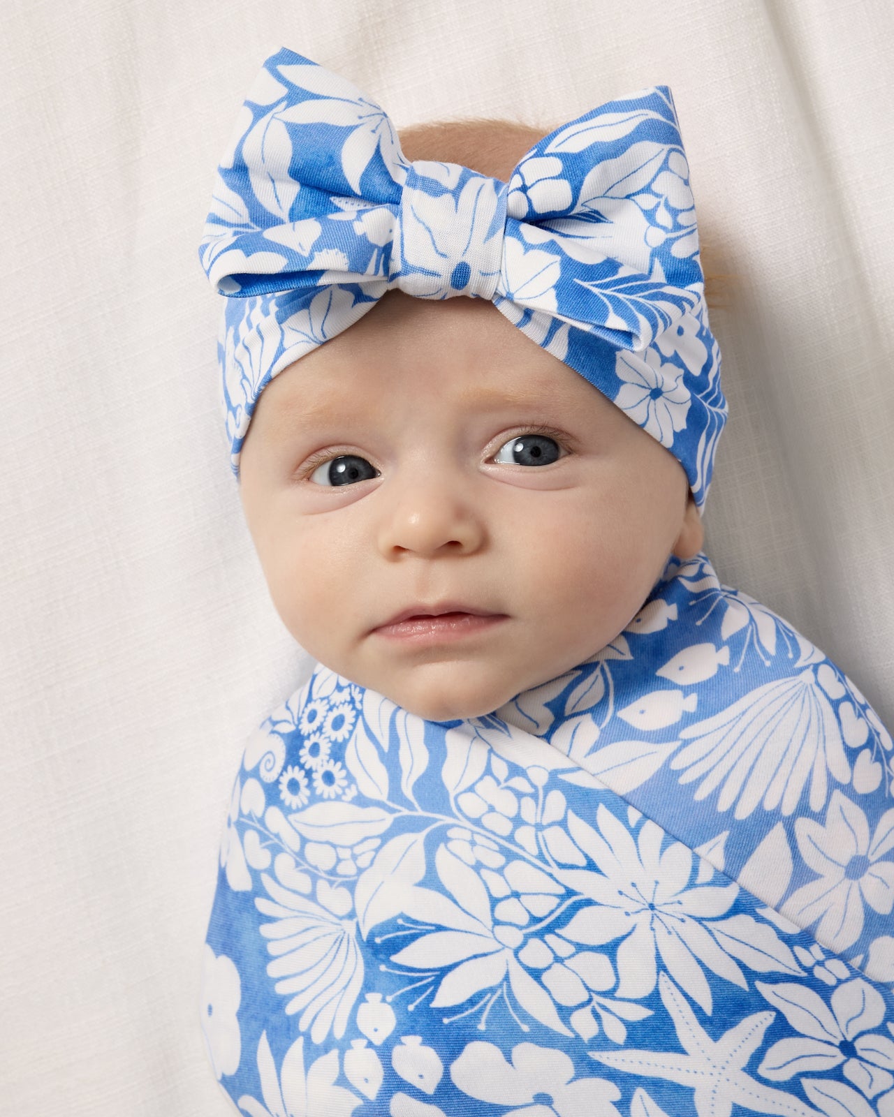 Close up of baby wrapped in the Azure Garden Swaddle & Luxe Bow Headband Set