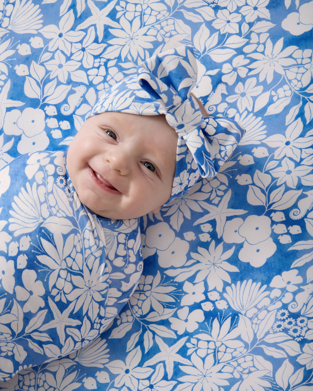 Close up of baby laying on the Azure Garden Fitted Crib Sheet wrapped in a matching swaddle