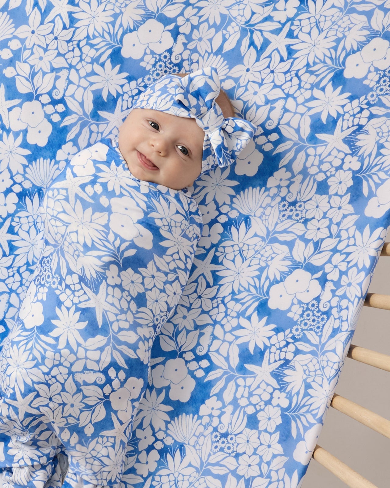 Overhead shot of baby laying on the Azure Garden Fitted Crib Sheet in a matching swaddle