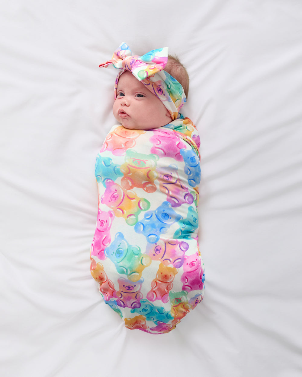Aerial view of newborn wrapped in the Gummy Giggles Swaddle & Luxe Bow Headband Set