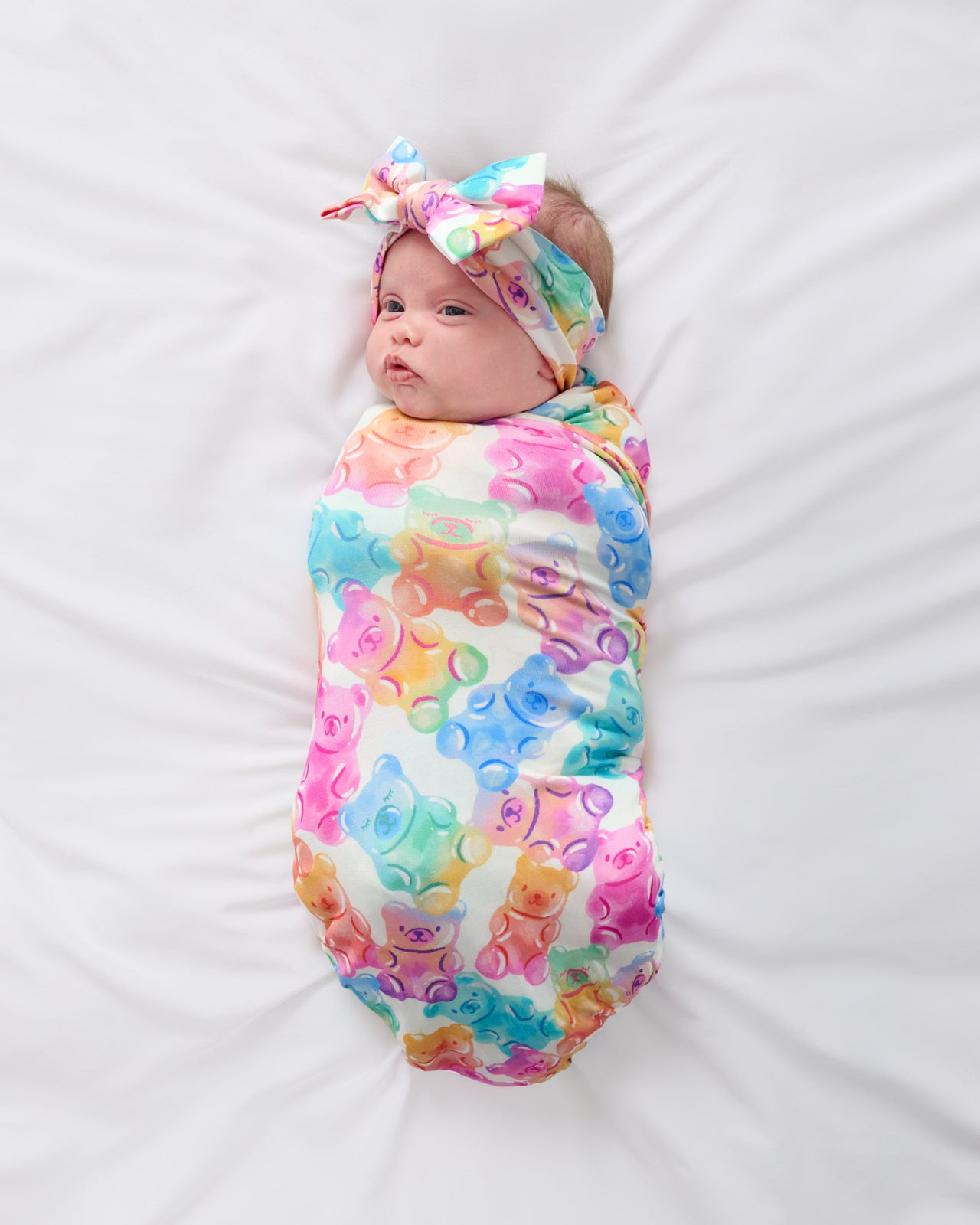Aerial view of newborn wrapped in the Gummy Giggles Swaddle & Luxe Bow Headband Set