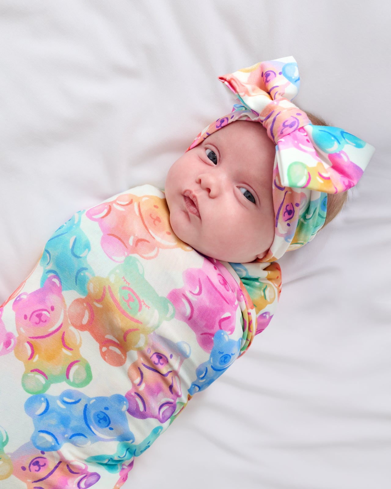 Close up of baby swaddled in the Gummy Giggles Swaddle & Luxe Bow Headband Set