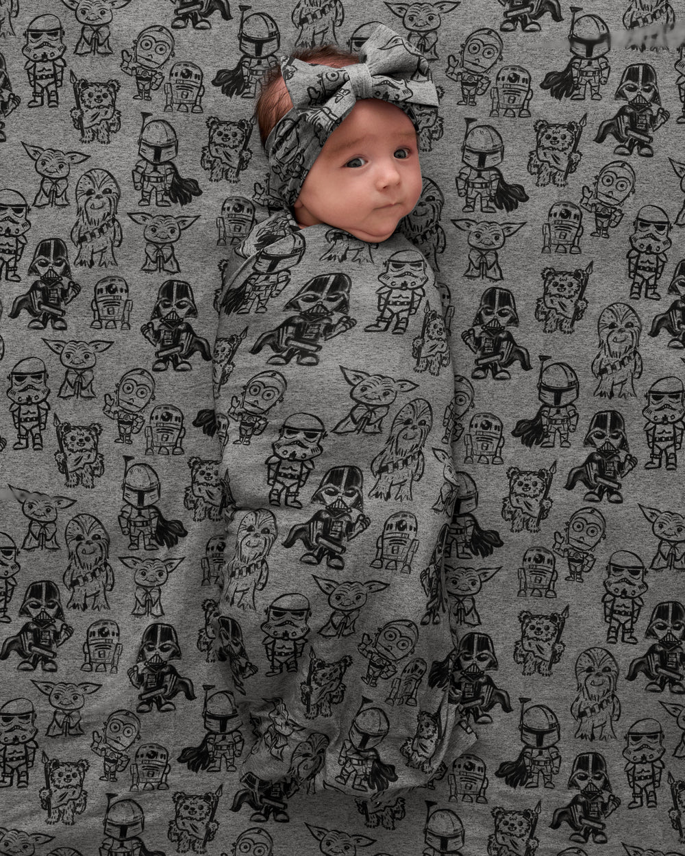 Overhead view of baby in the Star Wars Far, Far, Away Friends Swaddle & Luxe Bow Headband Set on a matching blanket