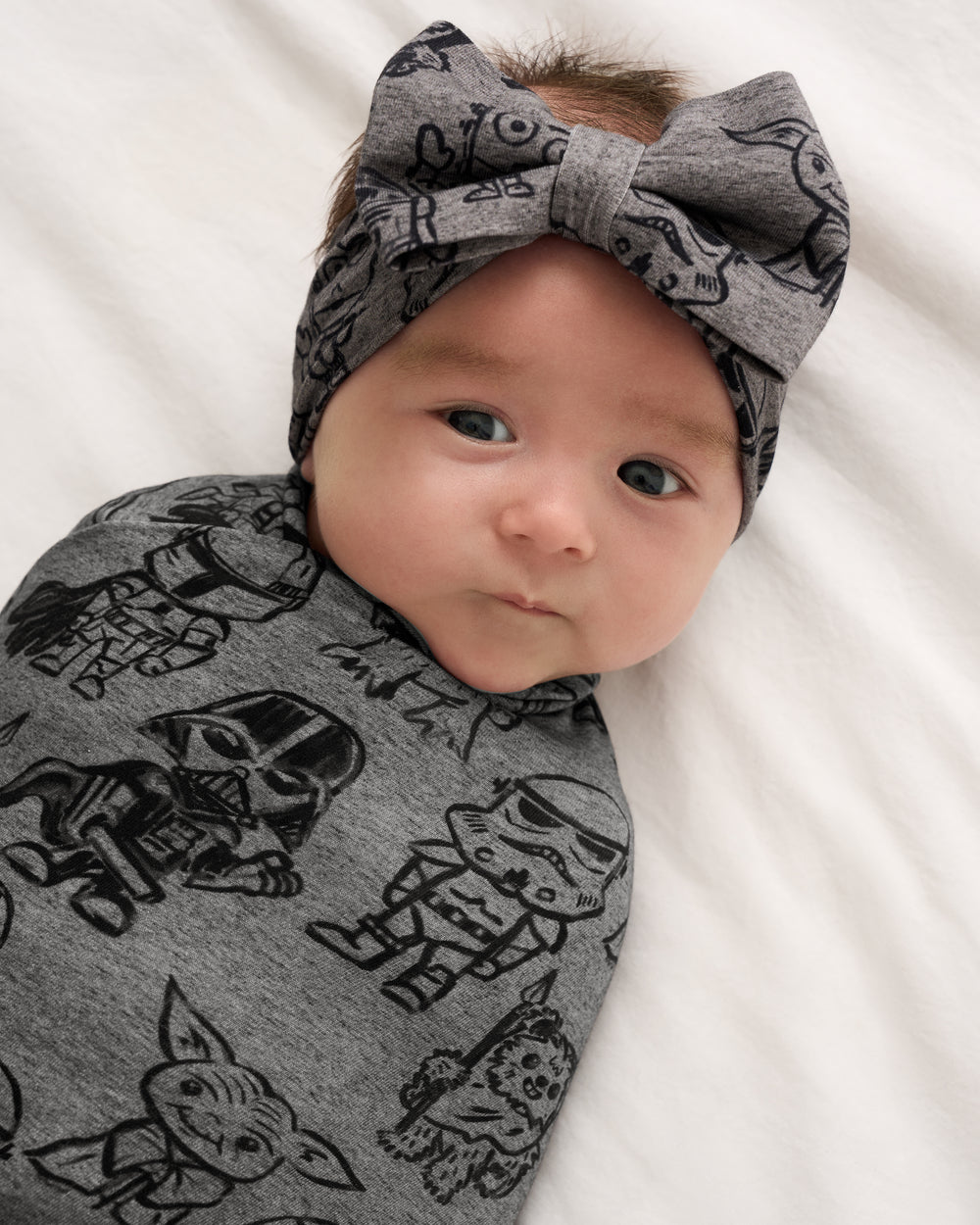 Close up of baby swaddled in the Star Wars Far, Far, Away Friends Swaddle & Luxe Bow Headband Set