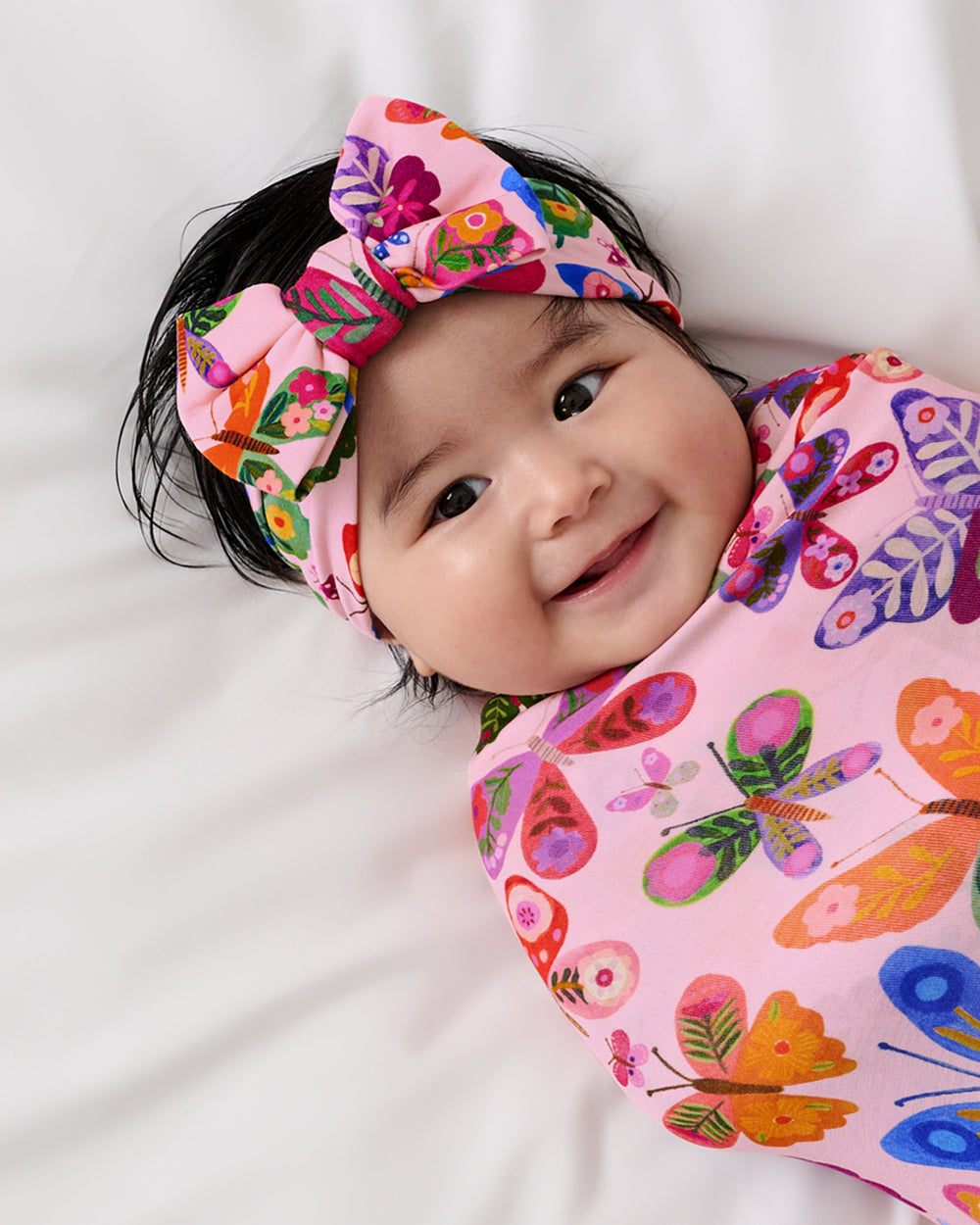 Close up of baby wrapped in the Flutter Garden Swaddle & Luxe Bow Headband Set