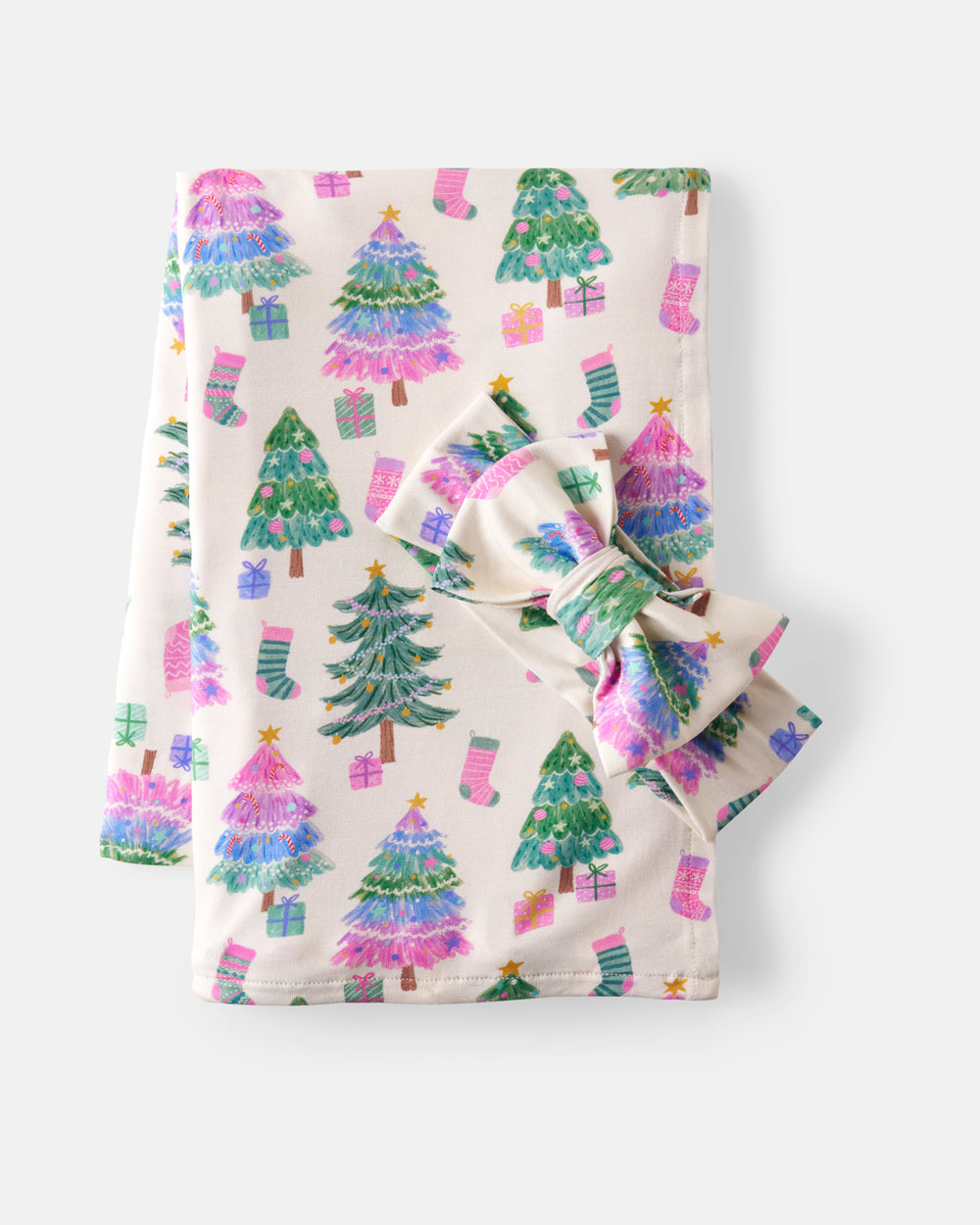A folded baby blanket with a matching bow, featuring a festive Christmas print of colorful pine trees, stockings, and presents on a cream background.