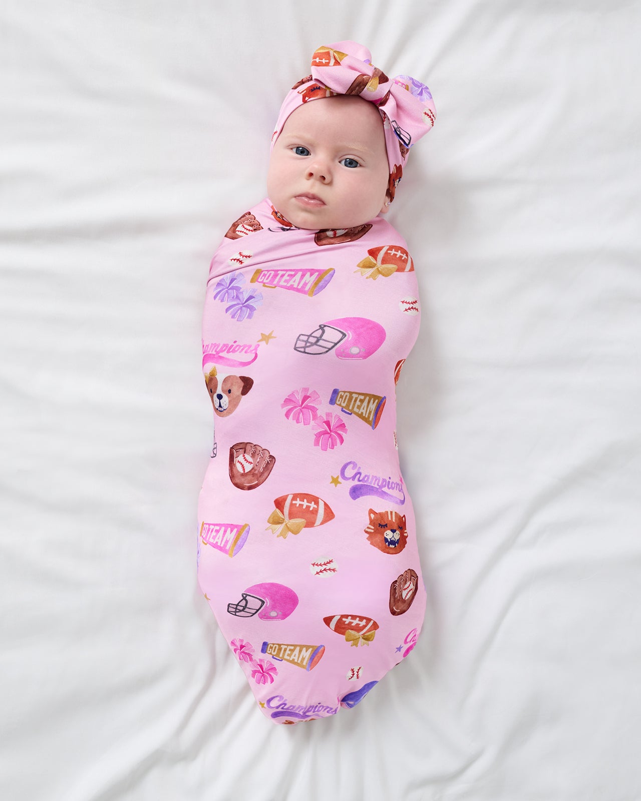Aerial view of newborn wrapped in the Team Spirit Pink Swaddle & Luxe Bow Headband Set