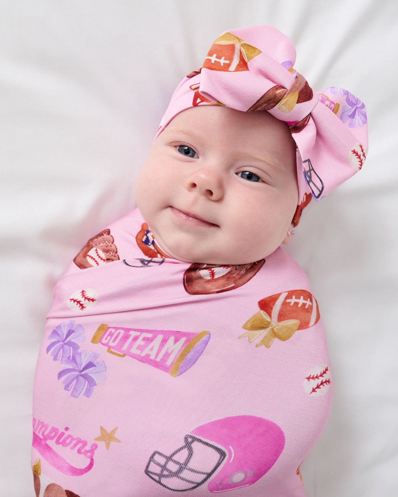 Close up of baby wearing the Team Spirit Pink Swaddle & Luxe Bow Headband Set